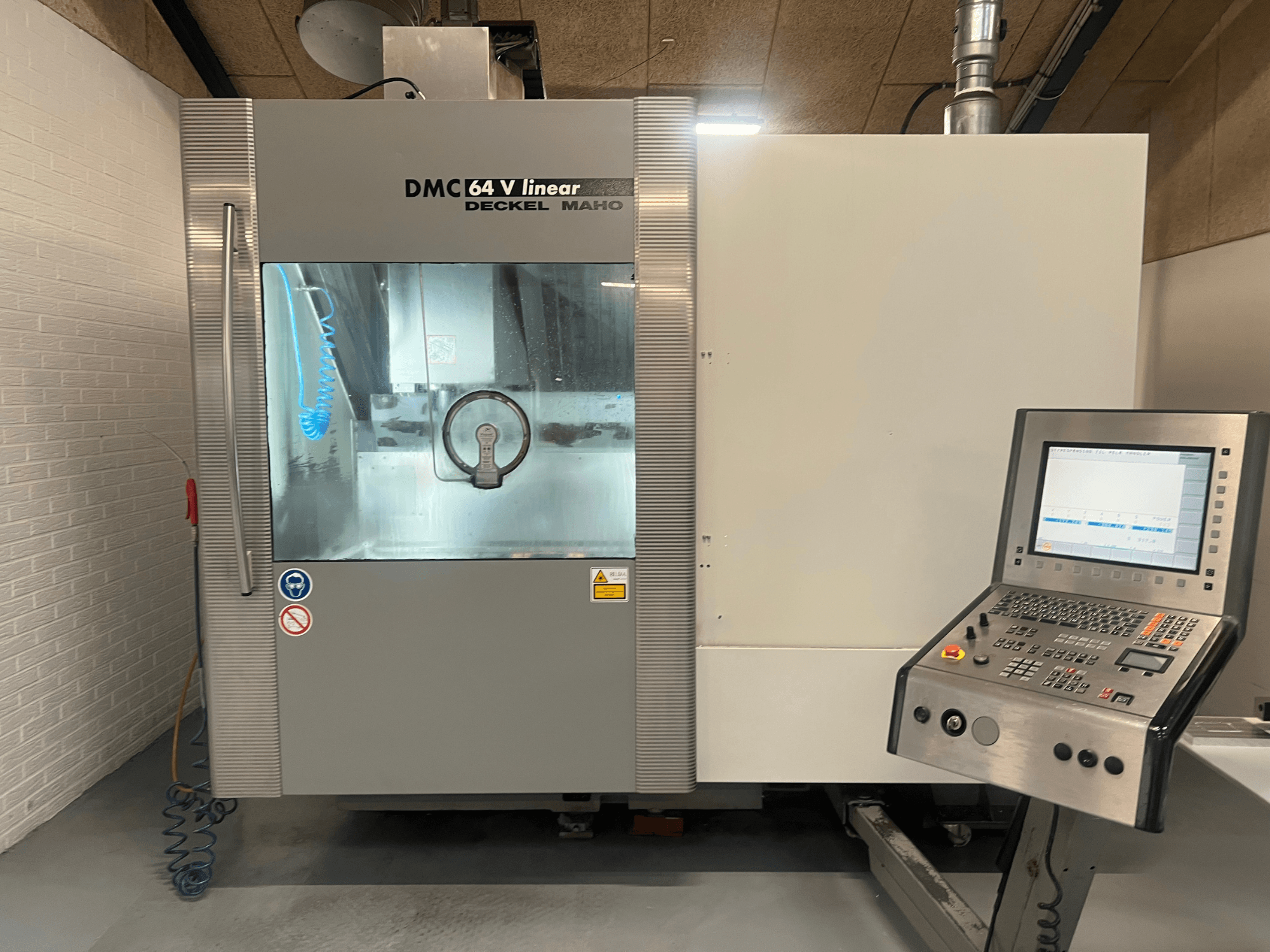 DMC 64 V Linear by Deckel Maho, CNC-työstökeskuksen etukuva, jossa ohjauspaneeli ja jäähdytysnesteen suutin näkyvissä.