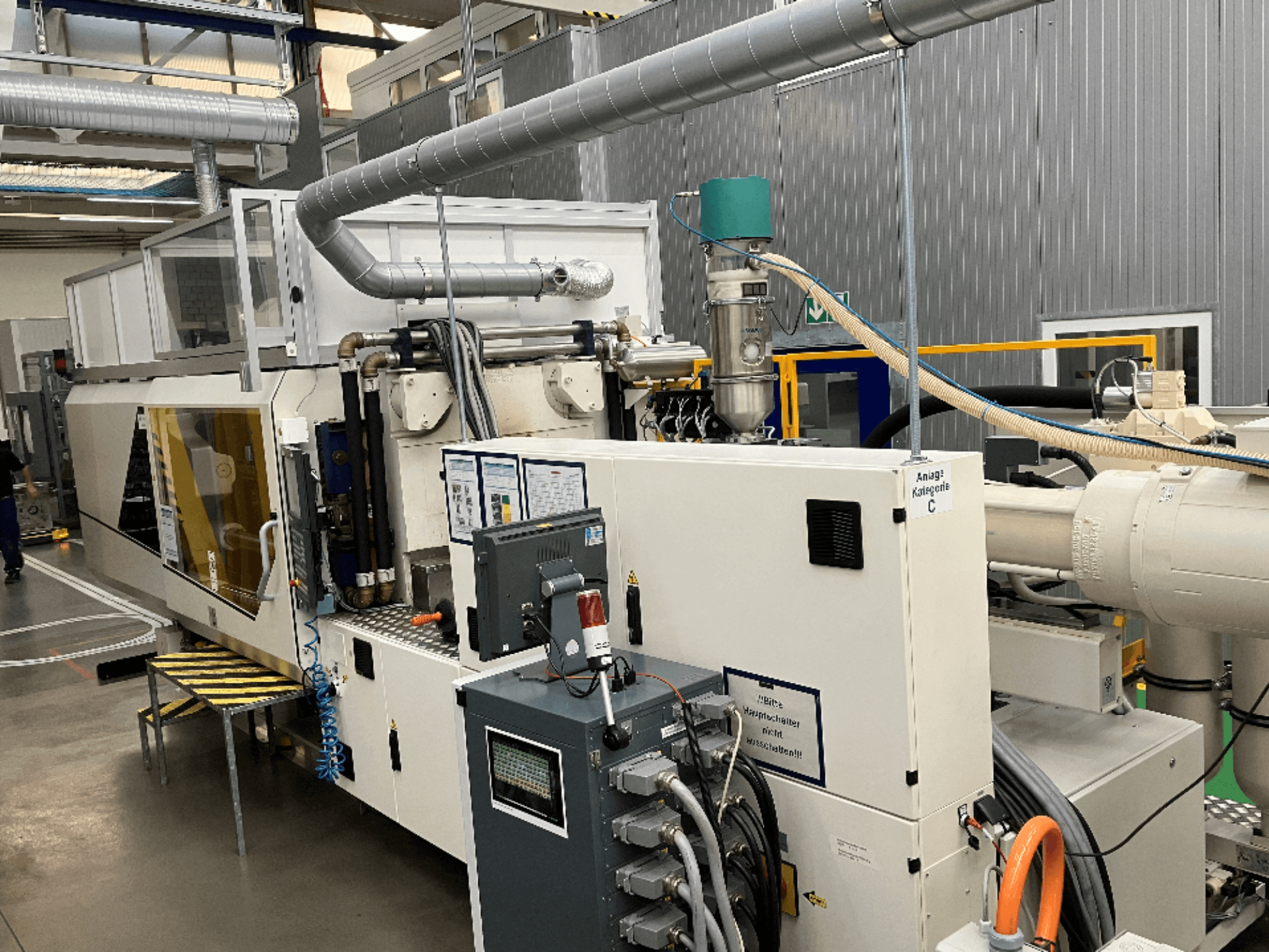 Ruiskuvalukone, etukuva, jossa tuotemerkin etiketti, ohjauspaneeli ja näkyvät letkut tehdasympäristössä.