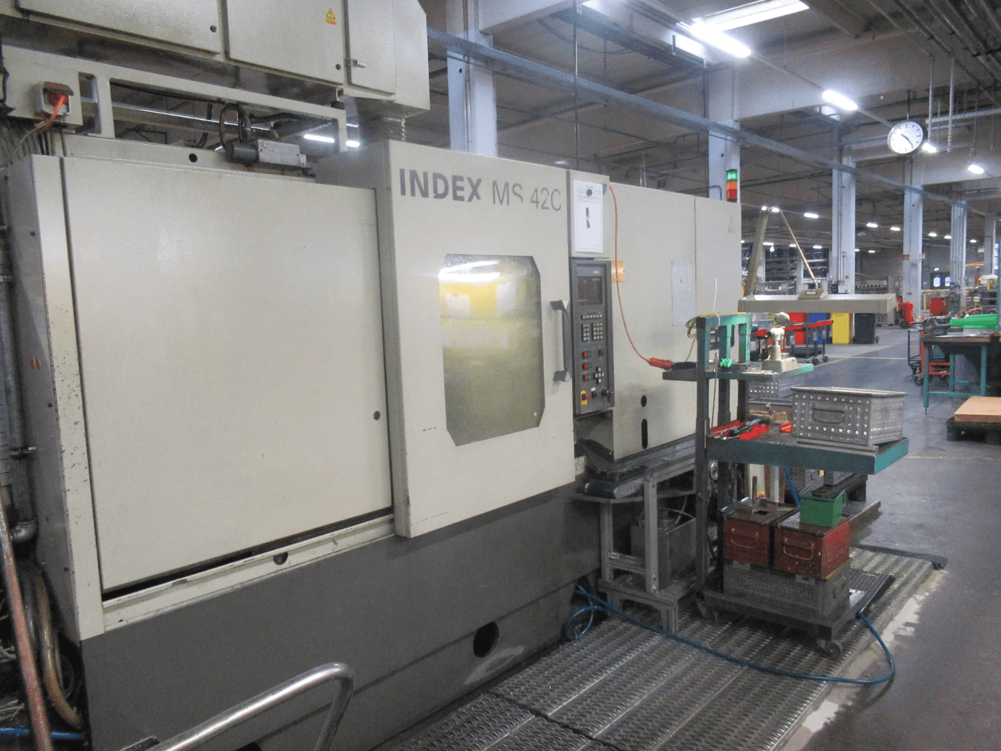 INDEX MS 42C CNC-kone työpajassa, sivukuva, jossa näkyy ohjauspaneeli ja työkalujen säilytys pyöräkärryllä.