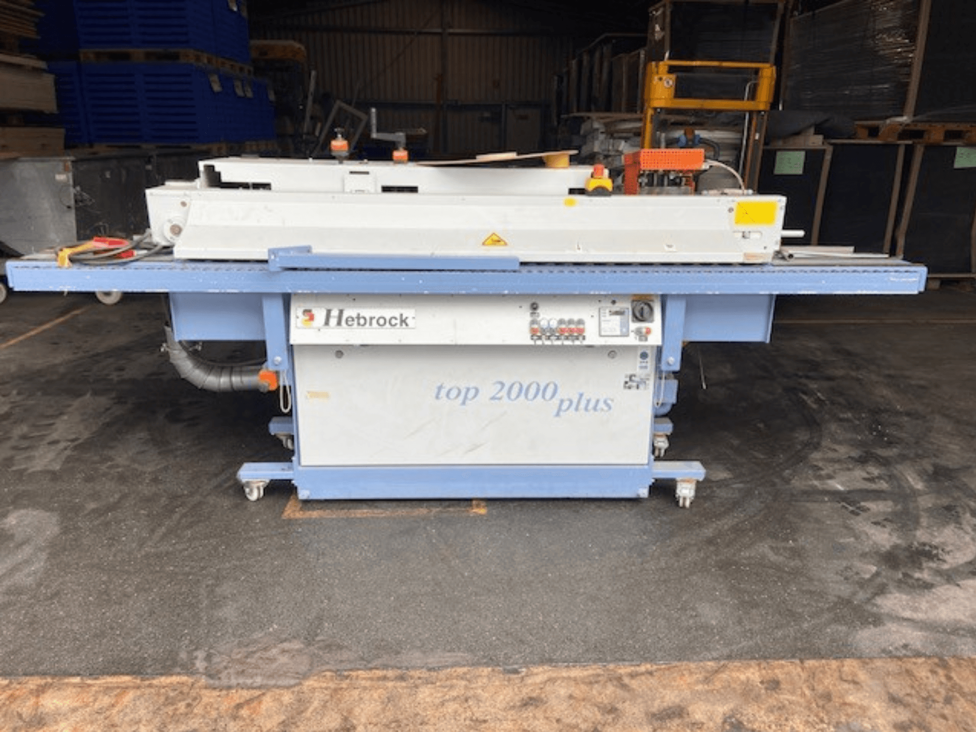 Hebrock Top 2000 Plus, etukuva; sähkökäyttöinen teollisuuskone, jossa on ohjauspaneeli, pyörät liikuteltavaksi ja turvatarrat näkyvissä.