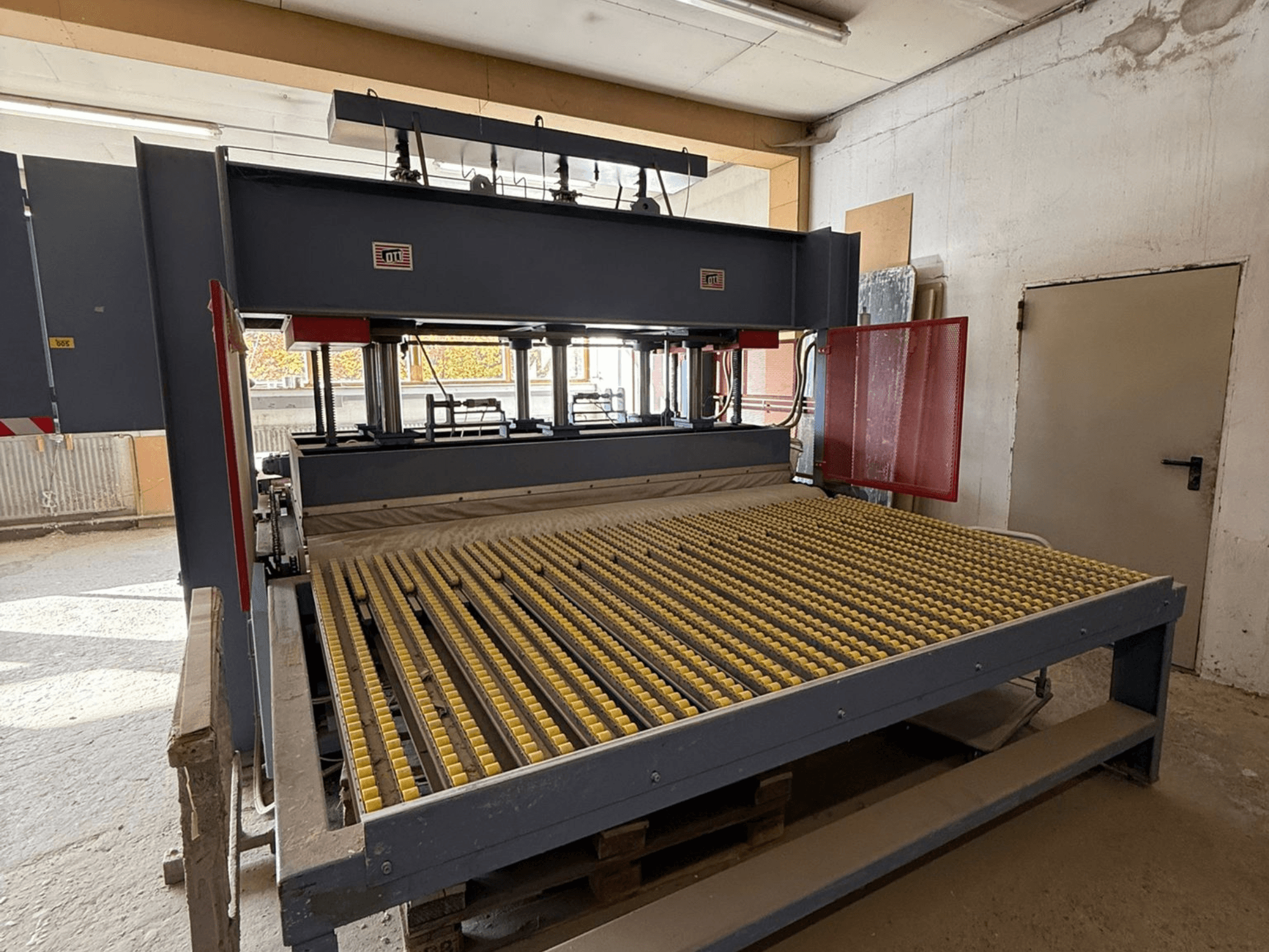 Teollisuuskone, jossa on keltaiset rullat, etukuva, tuotemerkin logo näkyvissä, käytetään materiaalien käsittelyyn työpajassa.