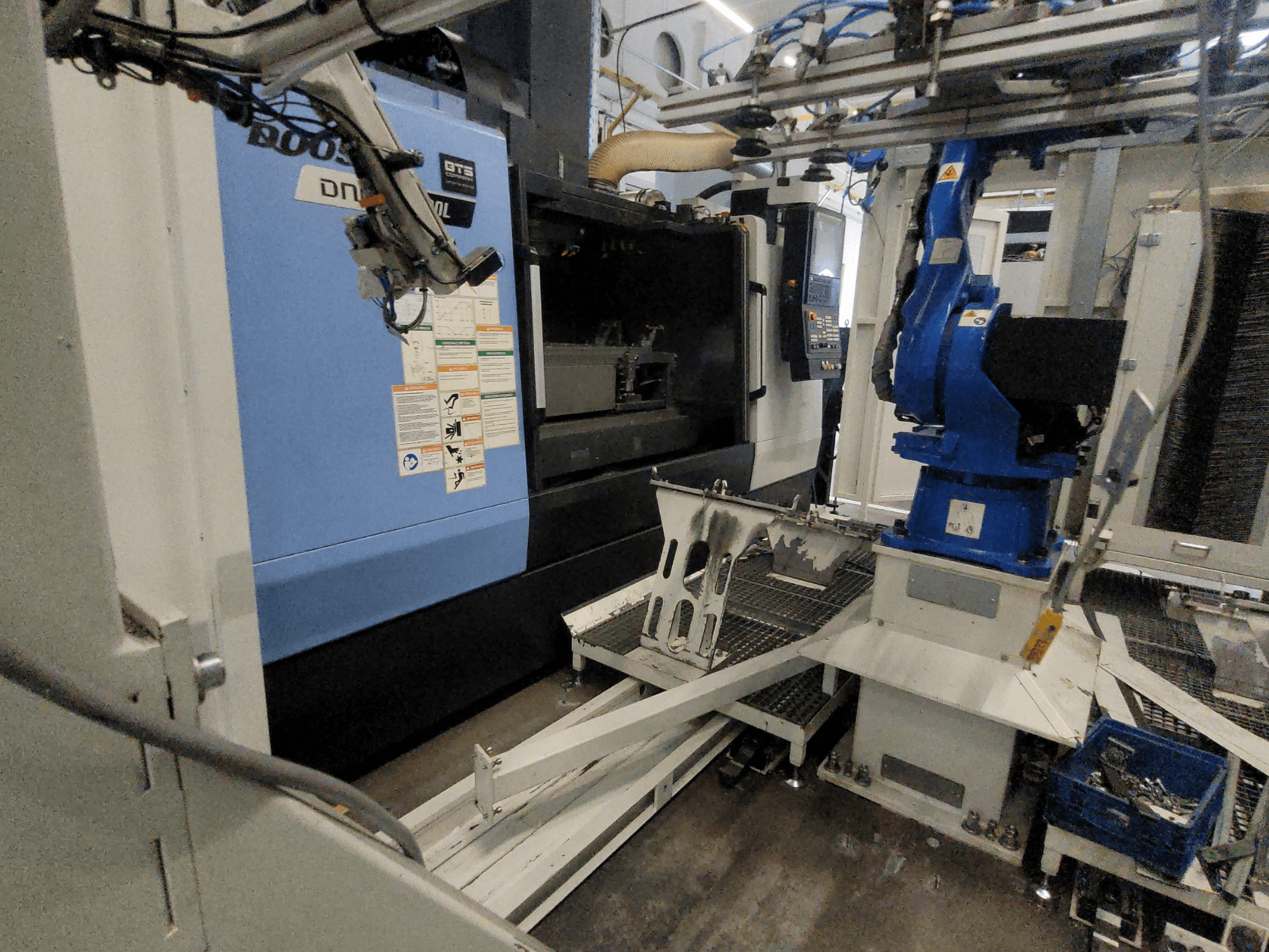 DOOSAN DNM 6700L -pystykoneistuskeskus sivulta katsottuna; kuvassa näkyvät robottivarsi ja ohjauspaneeli, jotka esittelevät koneen kokoonpanon.