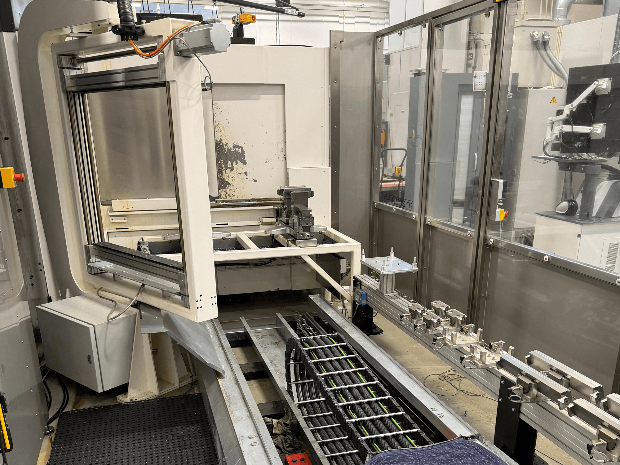 Automatisoitu teollinen työasema, jossa robottivarsi, kiskojärjestelmä ja ohjauspaneeli sivukuvassa.