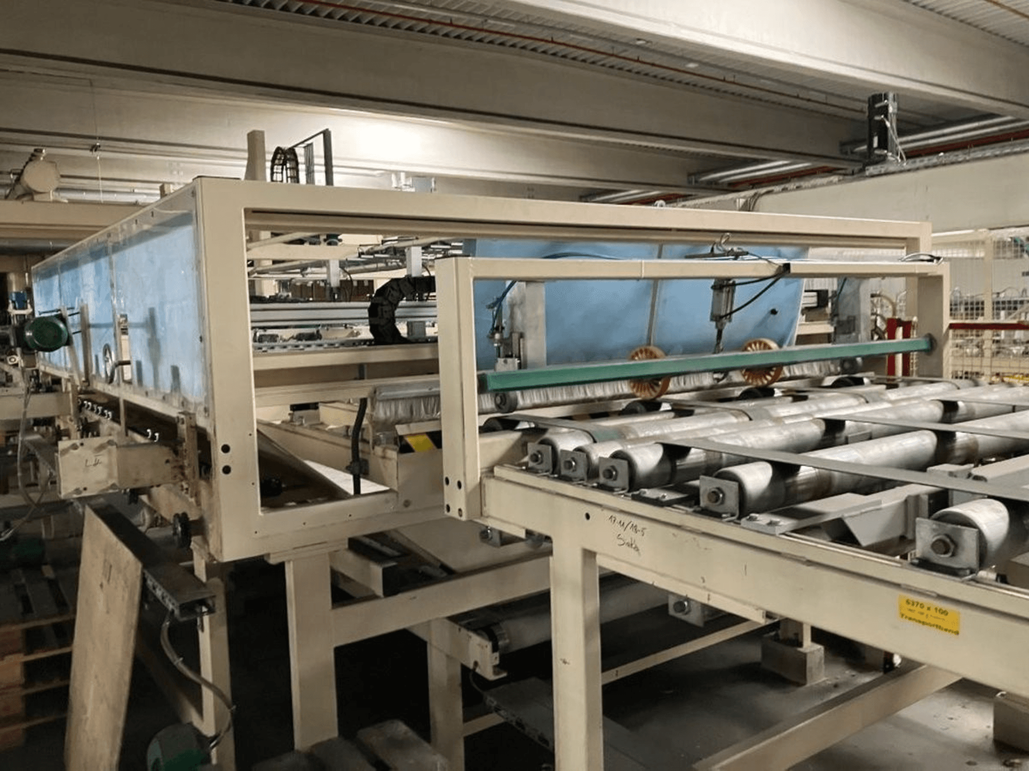 WEMHÖNER KT-F-1E laminointipuristin, sivukuva, jossa on rullat ja ohjaimet materiaalin käsittelyä varten tehdasympäristössä.