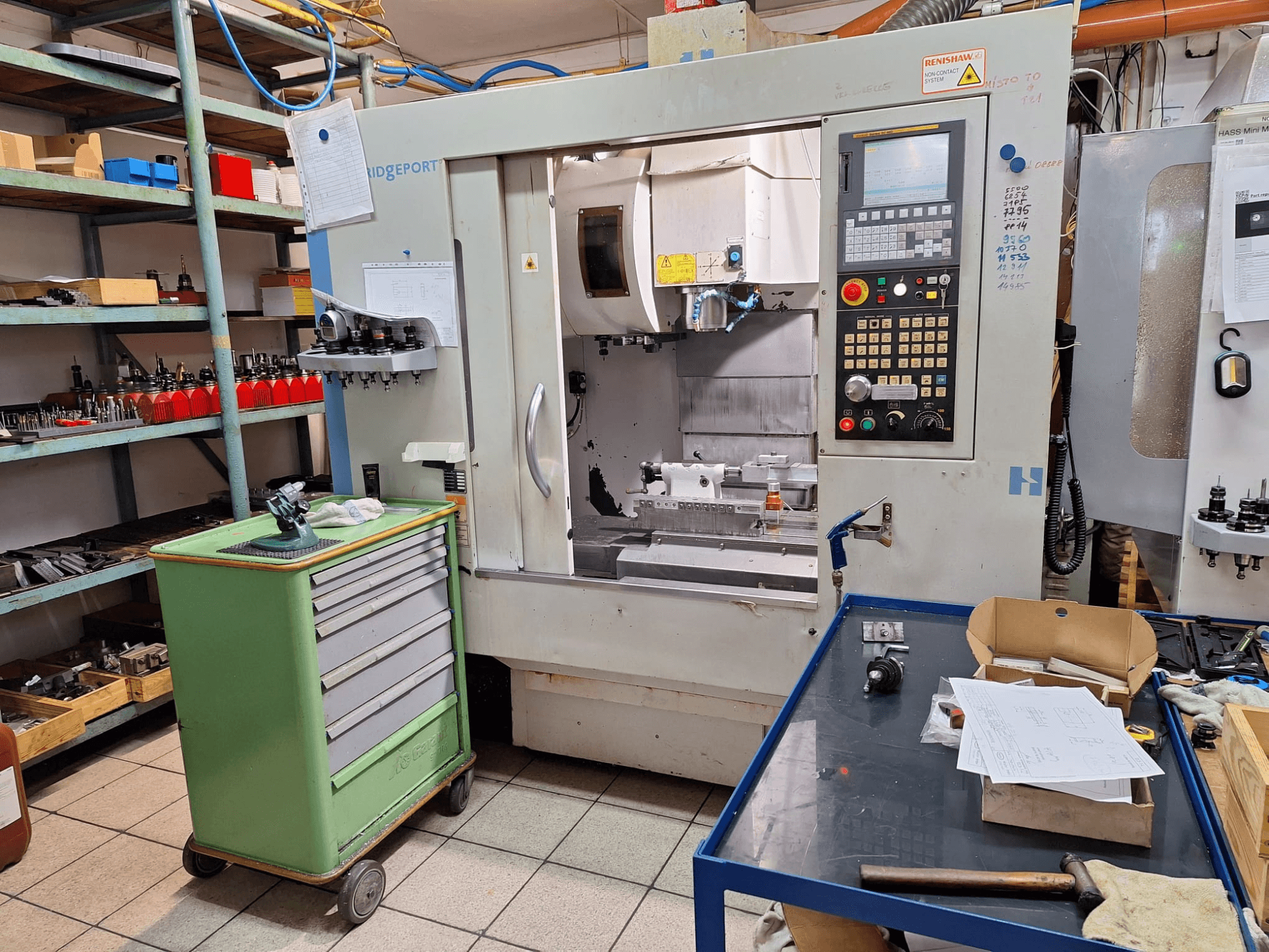 Hardinge Bridgeport GX 710 -pystykoneistuskeskus edestä katsottuna, ohjauspaneeli, työkalut ja hyllyt työpajaympäristössä.