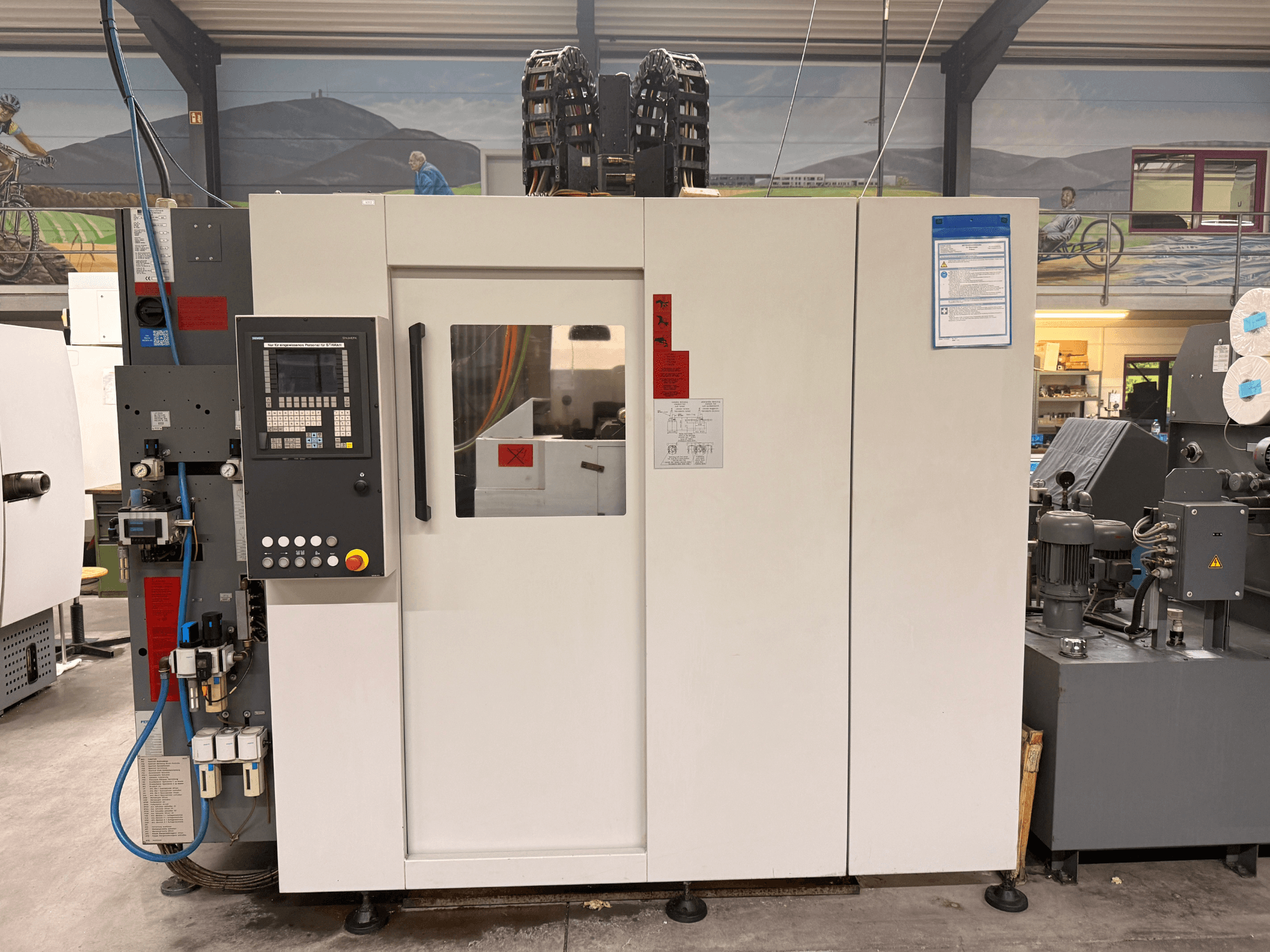 Valkoinen CNC-työstökeskus, jossa on ohjauspaneeli, etukuva, jossa on painikkeet ja digitaalinäyttö, työpajassa.