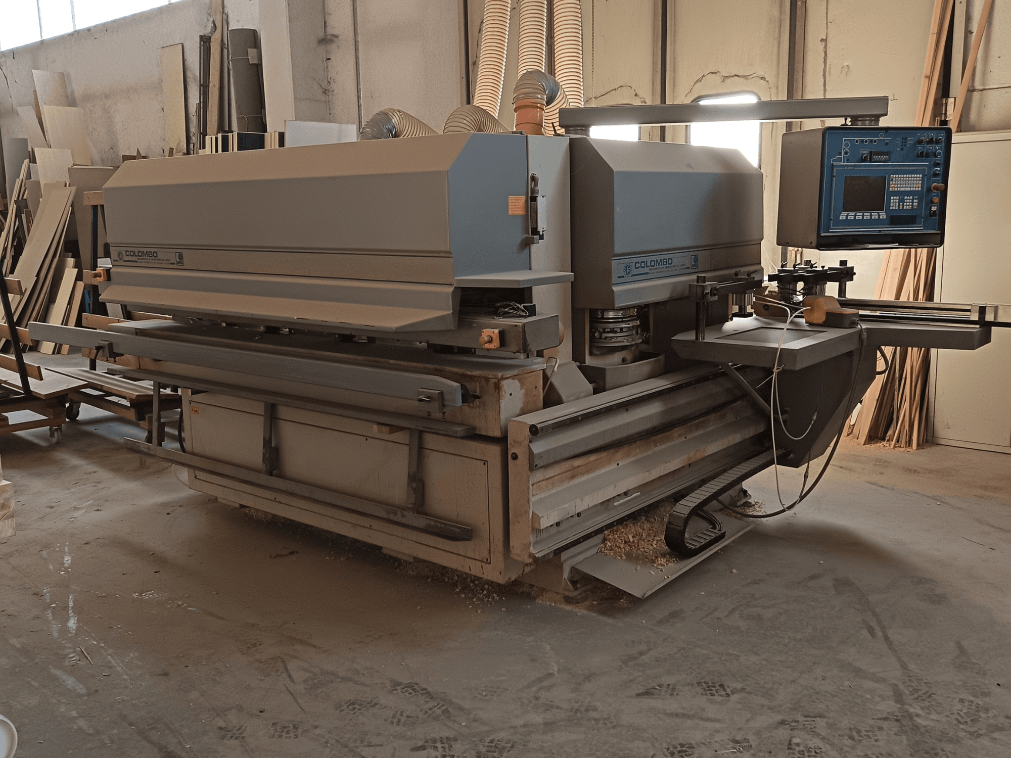 Colombon puuntyöstökone, sivukuva, jossa näkyy ohjauspaneeli, leikkuuterät ja sahauspölyn kerääntyminen työpajassa.