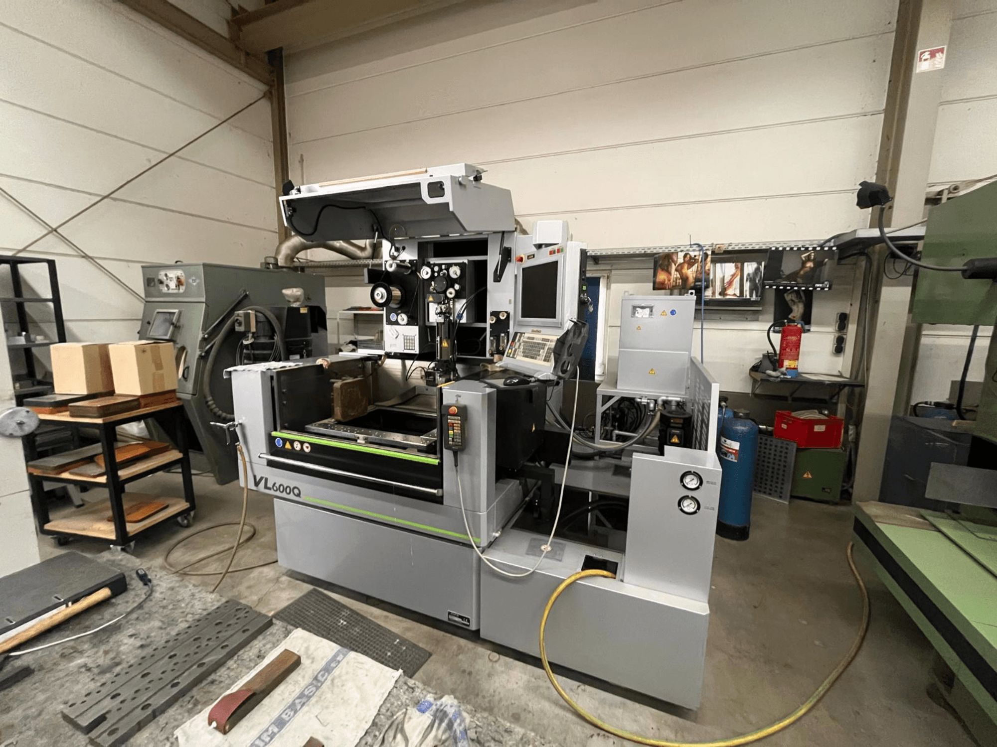 VL600Q CNC-kone työpajassa, etukuva, ohjauspaneeli, materiaali paikallaan ja erilaisia työkaluja lähellä.