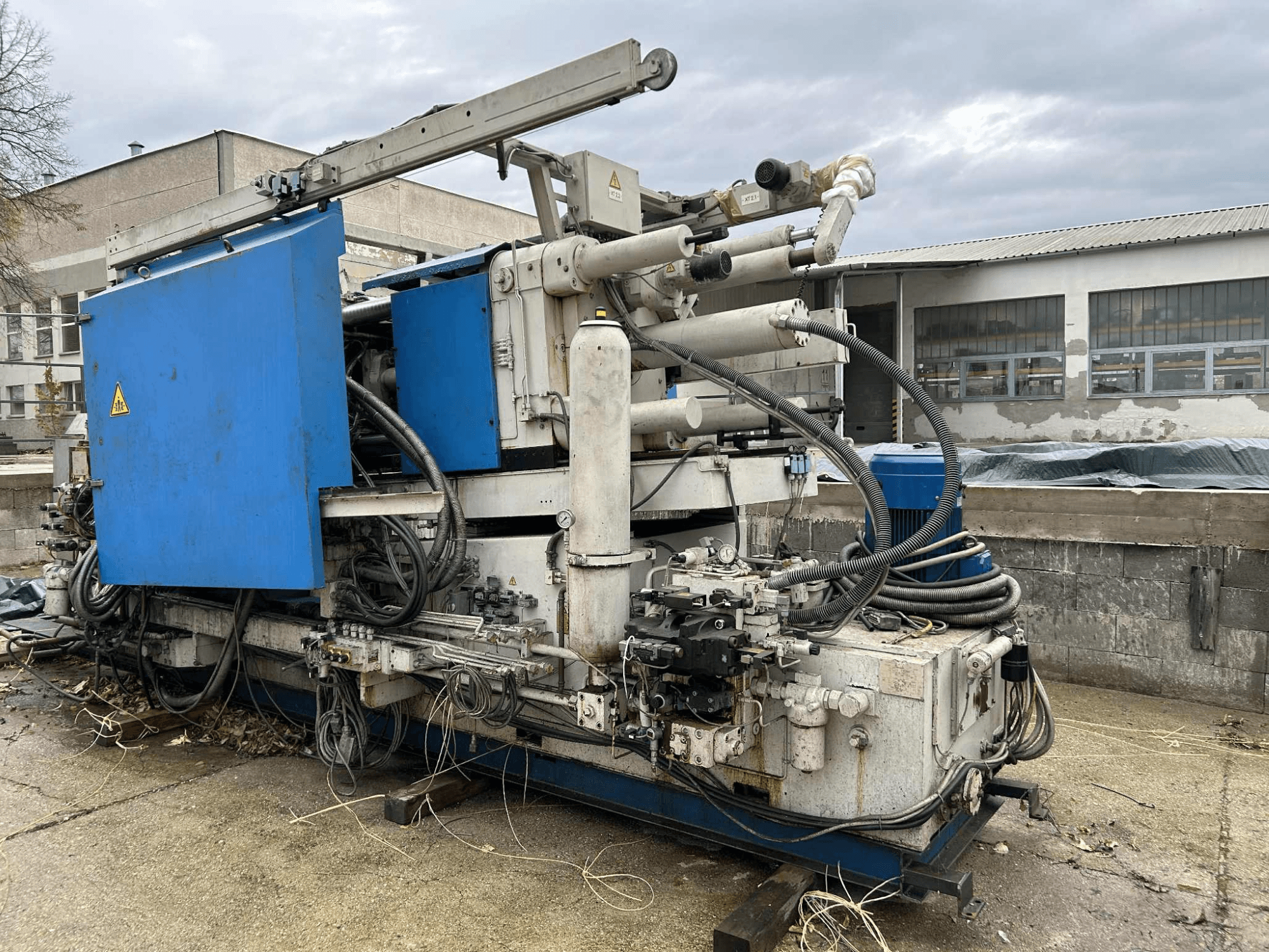 Suuri teollinen hydrauliikkakone, jossa on sininen kotelo, erilaisia letkuja ja metalliosia, sivulta katsottuna.