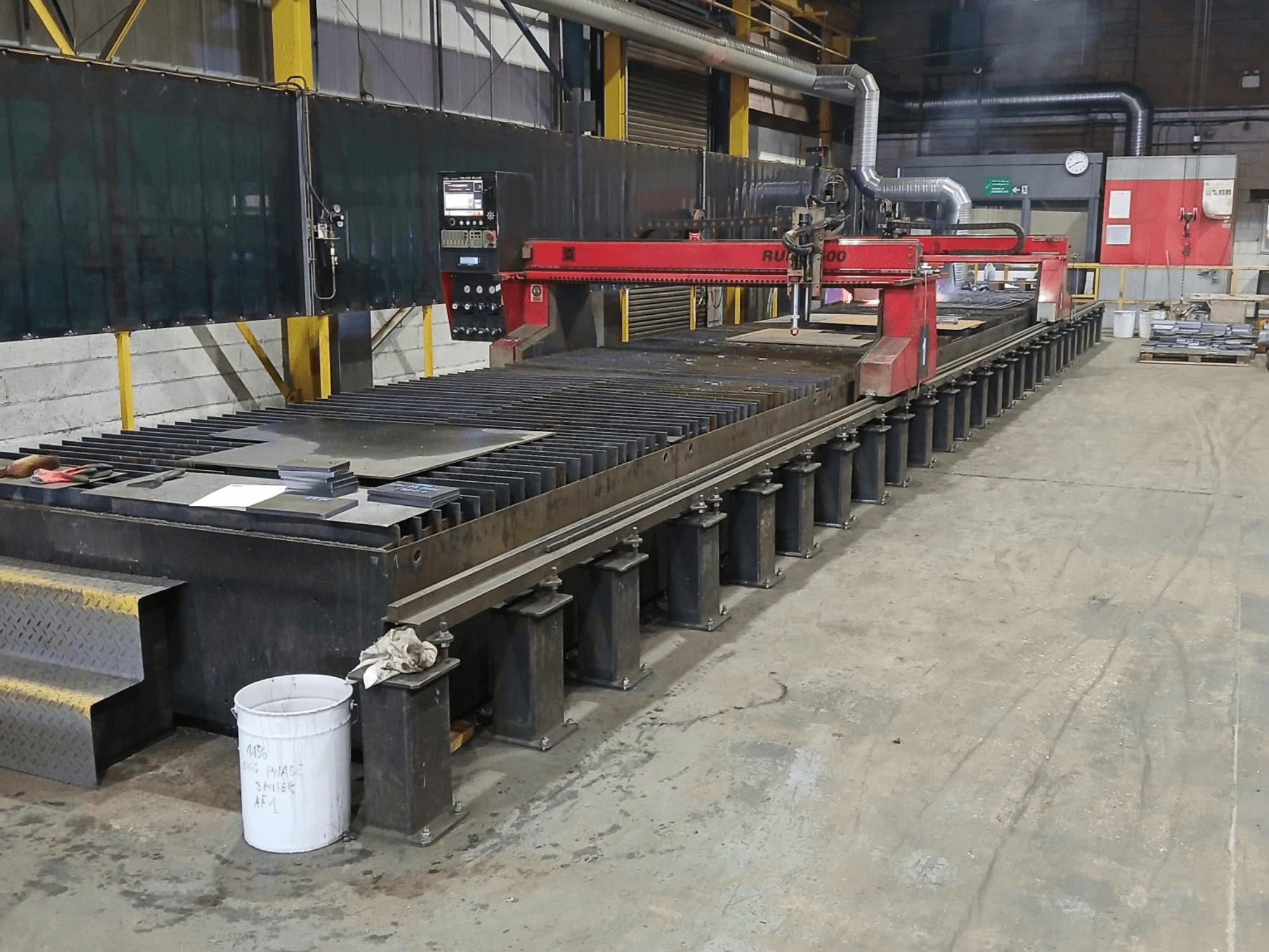 Punainen RUIDA 300 -leikkauskone, sivukuva, metallilevy teräspöydällä, teollisessa työtilassa.