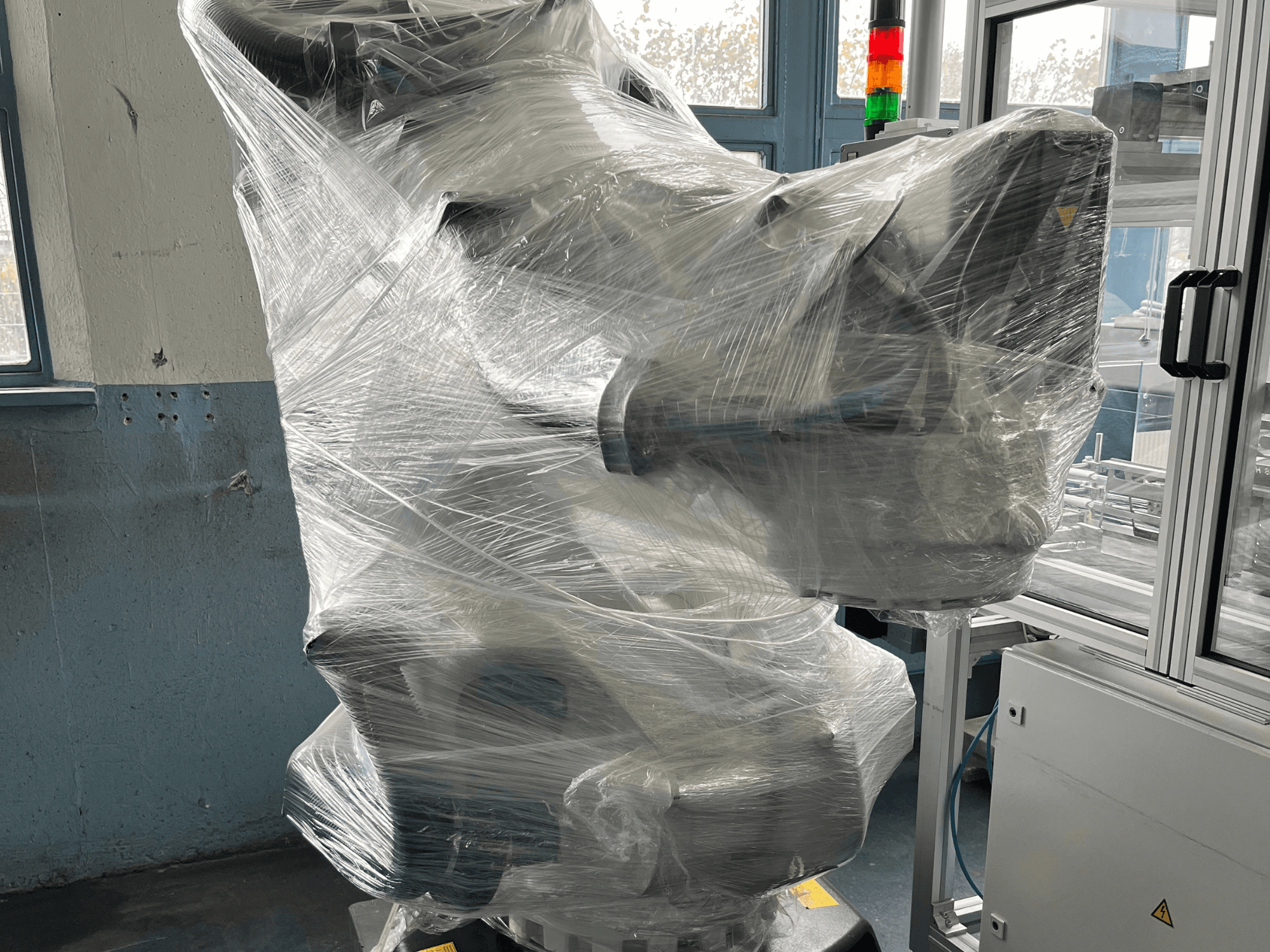 Muoviin kääritty teollisuusrobottikäsi, etukuva. Sisältää ohjausyksikön ja merkkivalon. Merkki ei ole näkyvissä.