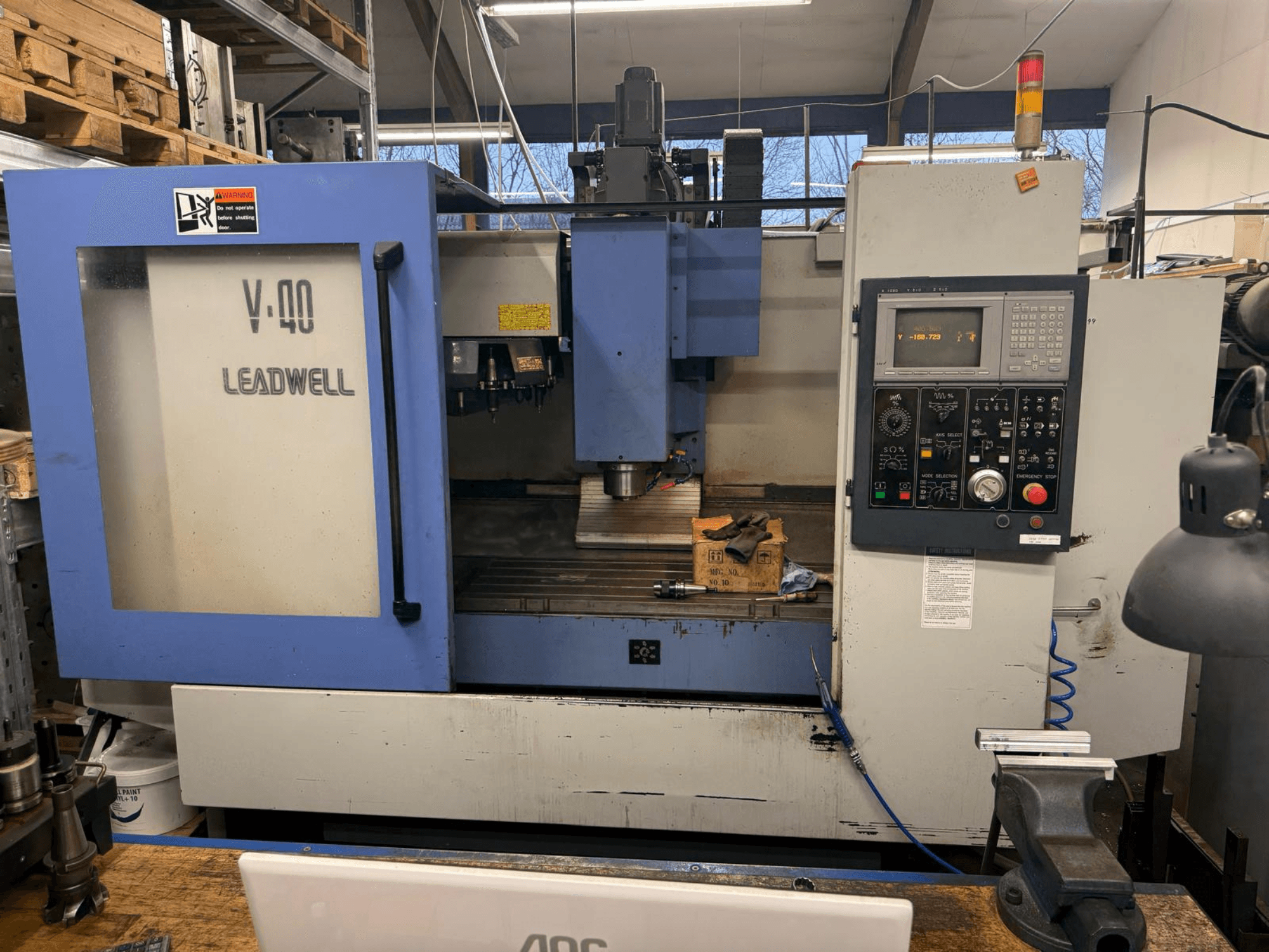 LEADWELL V-40 CNC-jyrsinkone, etukuva, jossa on ohjauspaneeli, leikkuutyökaluja ja ruuvipenkki työpöydällä.