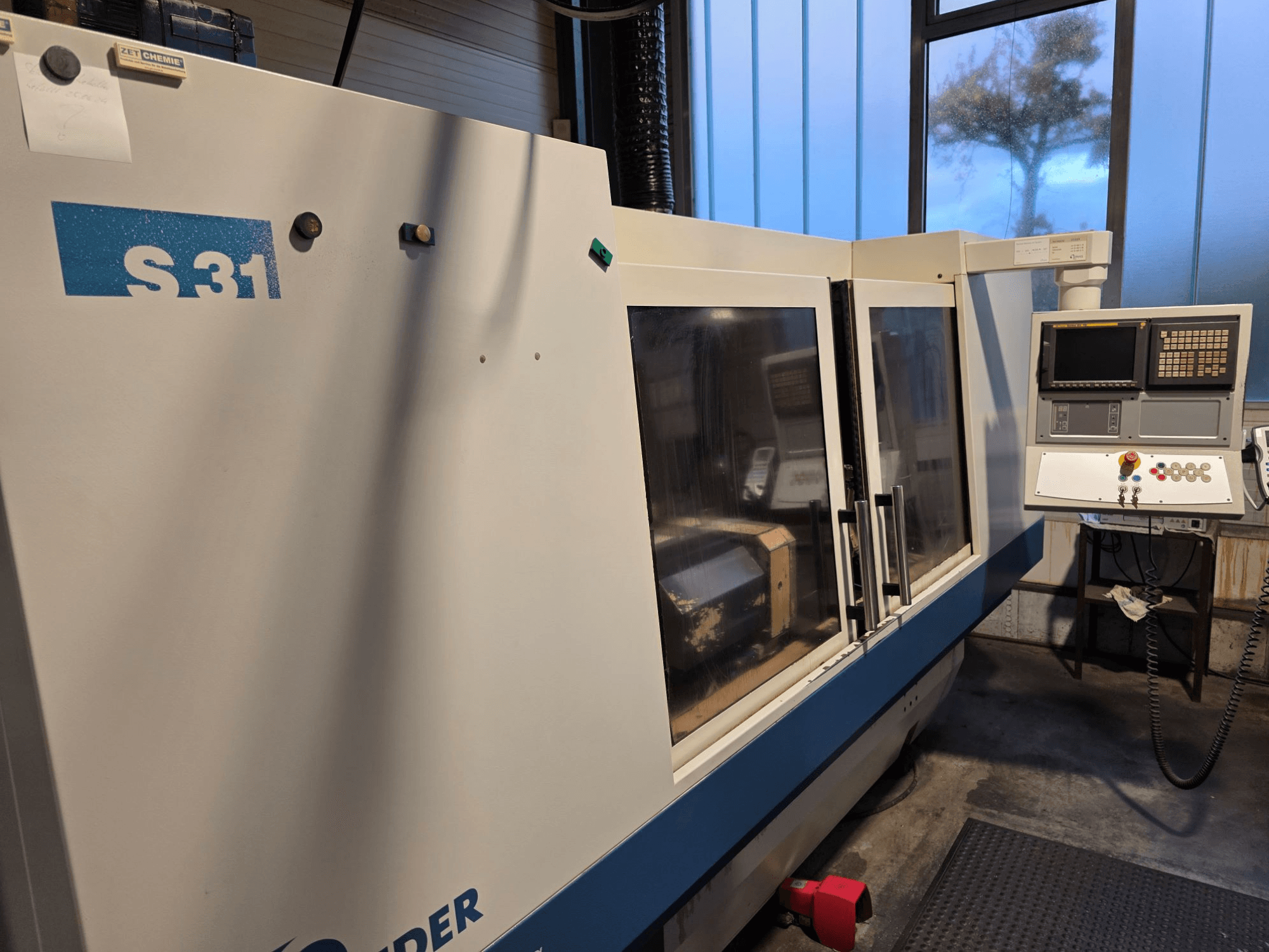 S31 CNC-hiomakone, etukuva, ohjauspaneeli, jossa näyttö ja painikkeet, suuri lasiovi, teollisuusympäristö.