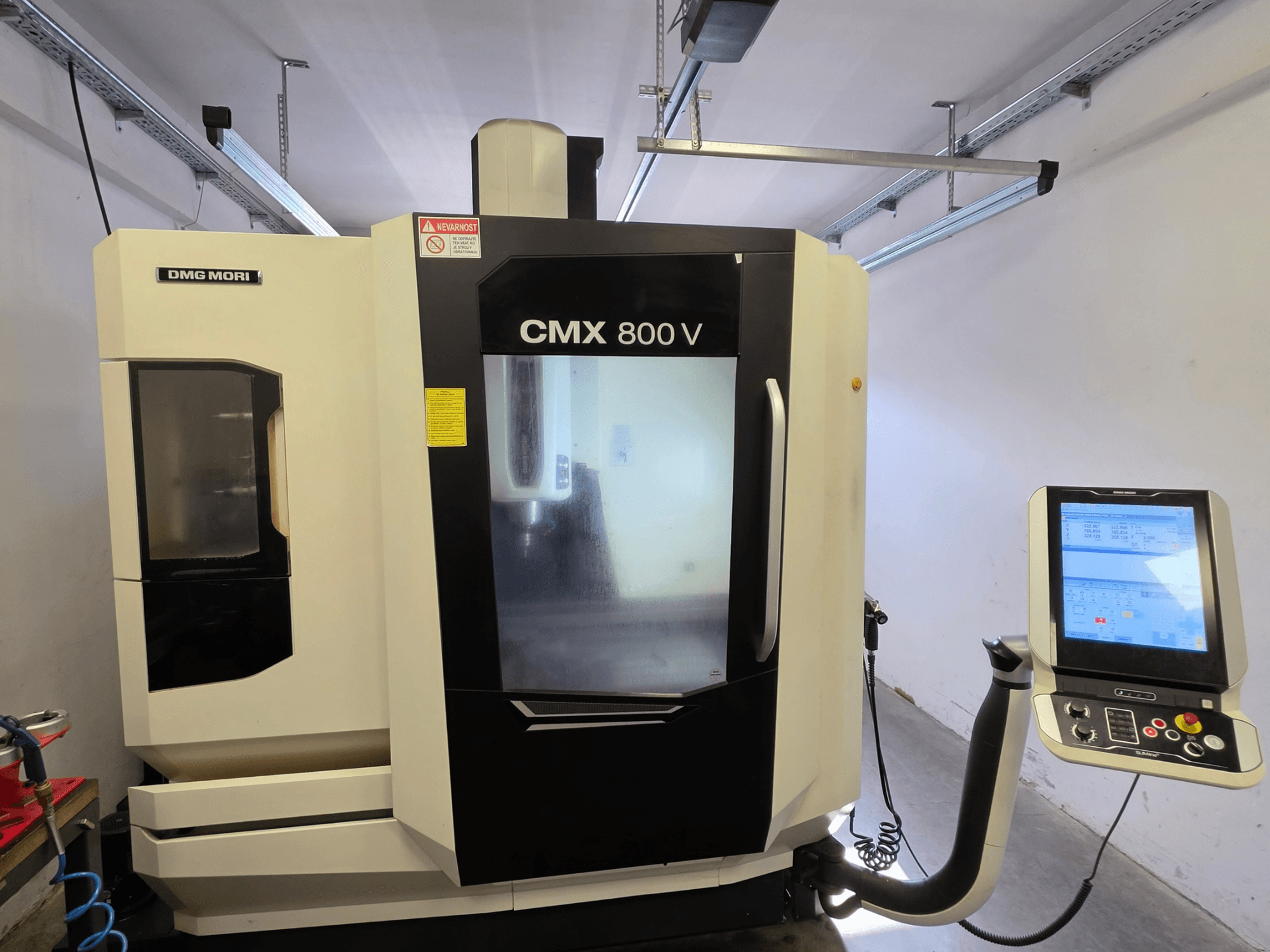 DMG MORI CMX 800V -pystykoneistuskeskus, etunäkymä, jossa on kosketusnäytöllinen ohjauspaneeli ja selkeät turvallisuusmerkinnät.
