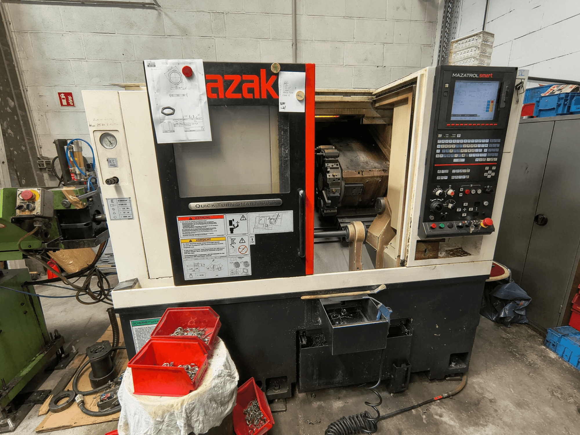 Mazak Quick Turn Smart 100 S, sivukuva, jossa näkyvät ohjauspaneeli, jäähdytysnesteen keräysastia sekä ruuvien säilytyslokerot.