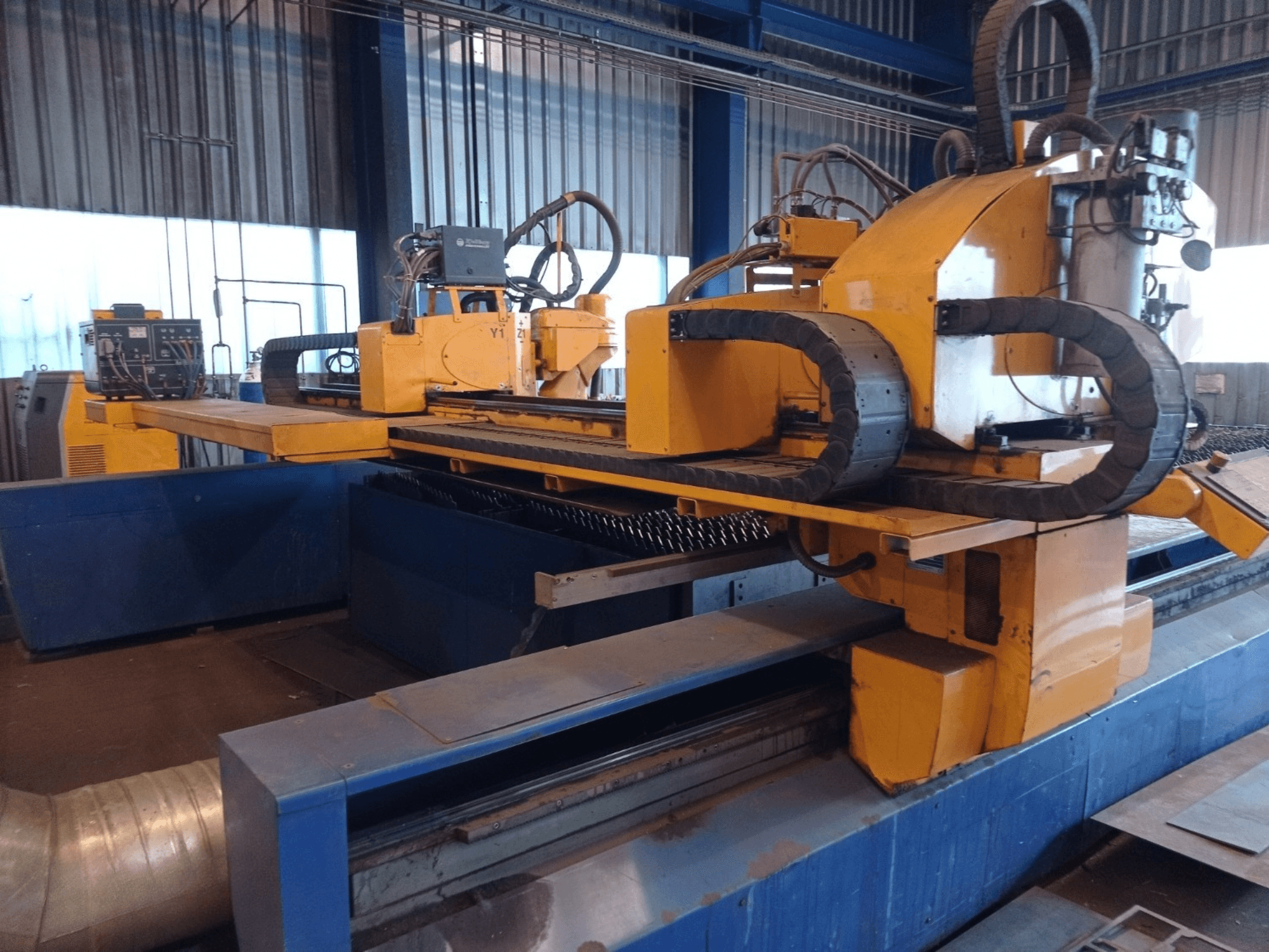 Keltainen CNC-plasmaleikkauskone, jossa on kaksi vaakasuoraa käsivartta, edestäpäin kuvattuna, ja jossa on ohjauspaneeli ja leikkaussänky.