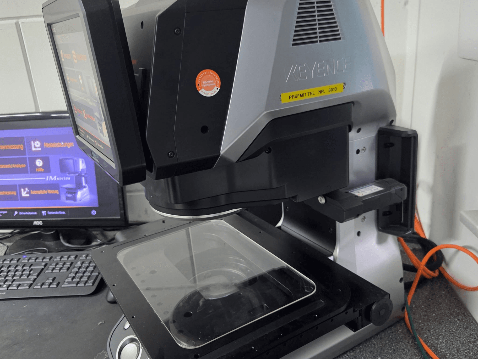 KEYENCE IM 7030 optinen mittauskone, etukuva, jossa on kosketusnäyttö ja lasinen mittauslevy.