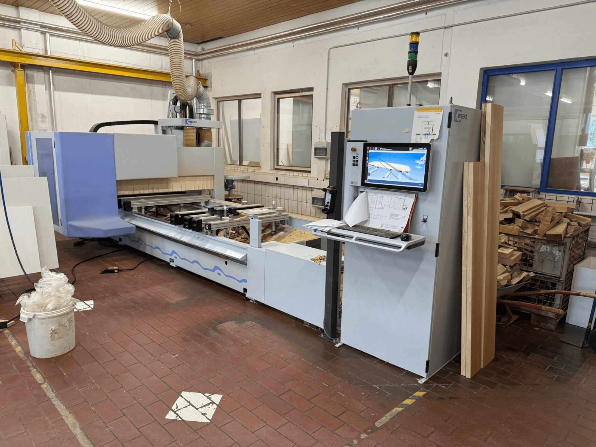 Weeke PROFI BMG211/32/12/K CNC-puunkäsittelykeskus, etunäkymä, jossa näkyy ohjauspaneeli ja puukappaleet sekä pölynpoistojärjestelmä.