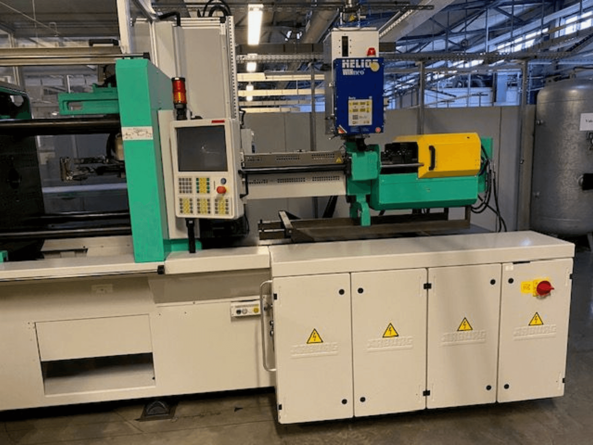 Teollinen ruiskuvalukone, malli HELIO, etukuva, jossa on ohjauspaneeli, suojukset ja hätäpysäytyspainike.