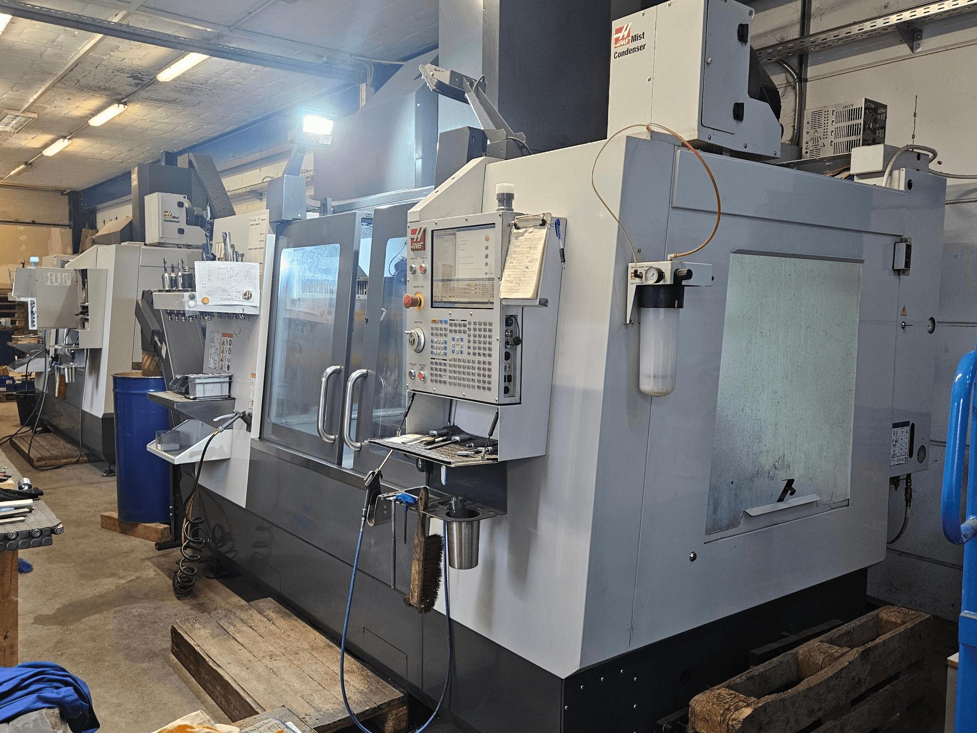 Haas VF-3YT/50 -pystykoneistuskeskus työpajassa; etunäkymä, jossa näkyvät ohjauspaneeli, työkalunpitimet ja sumun tiivistin.
