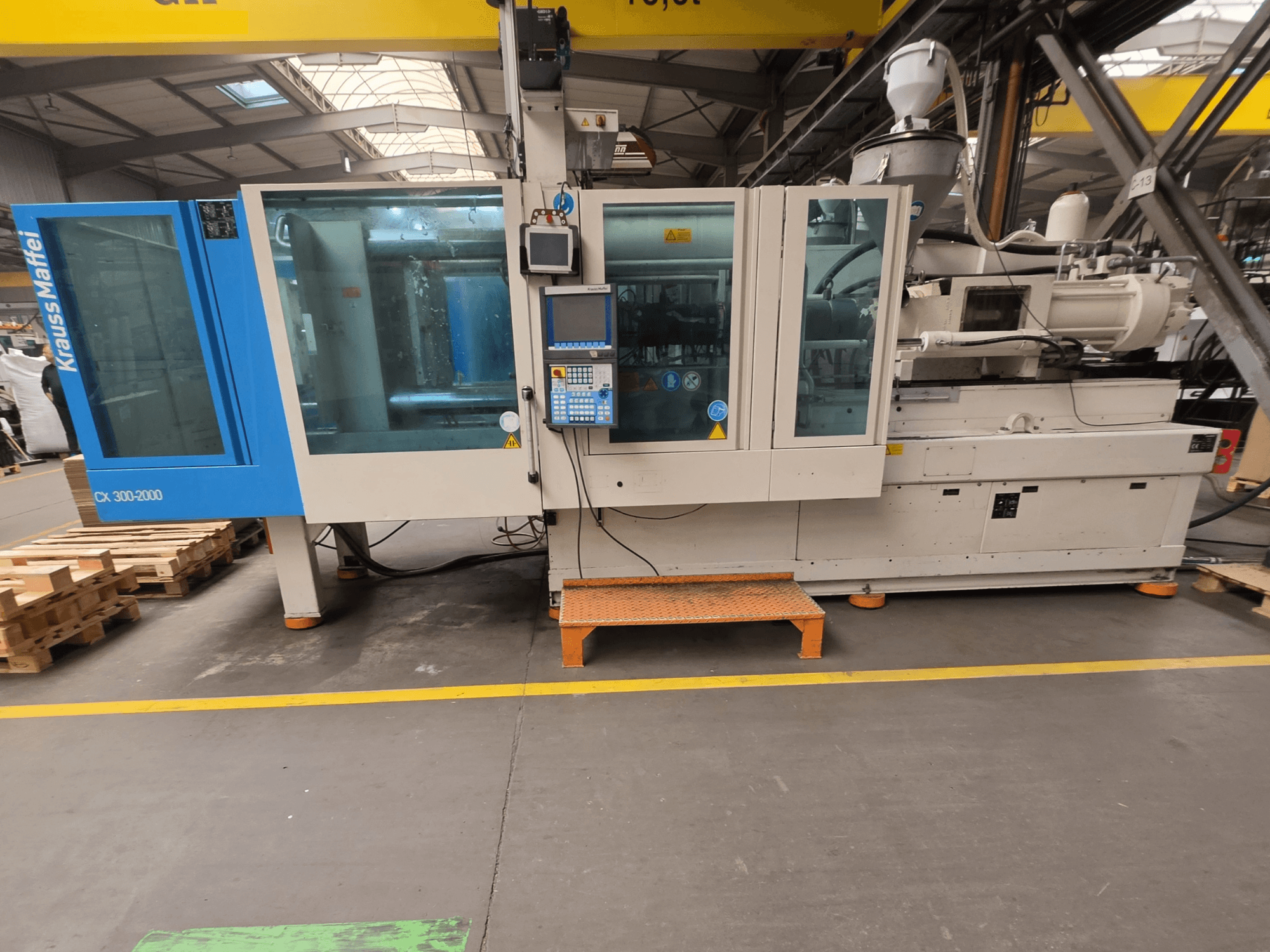 Krauss Maffei 300-2000 CX hydraulinen ruiskuvalukone, sivukuva, jossa näkyy ohjauspaneeli ja suuret ikkunat.