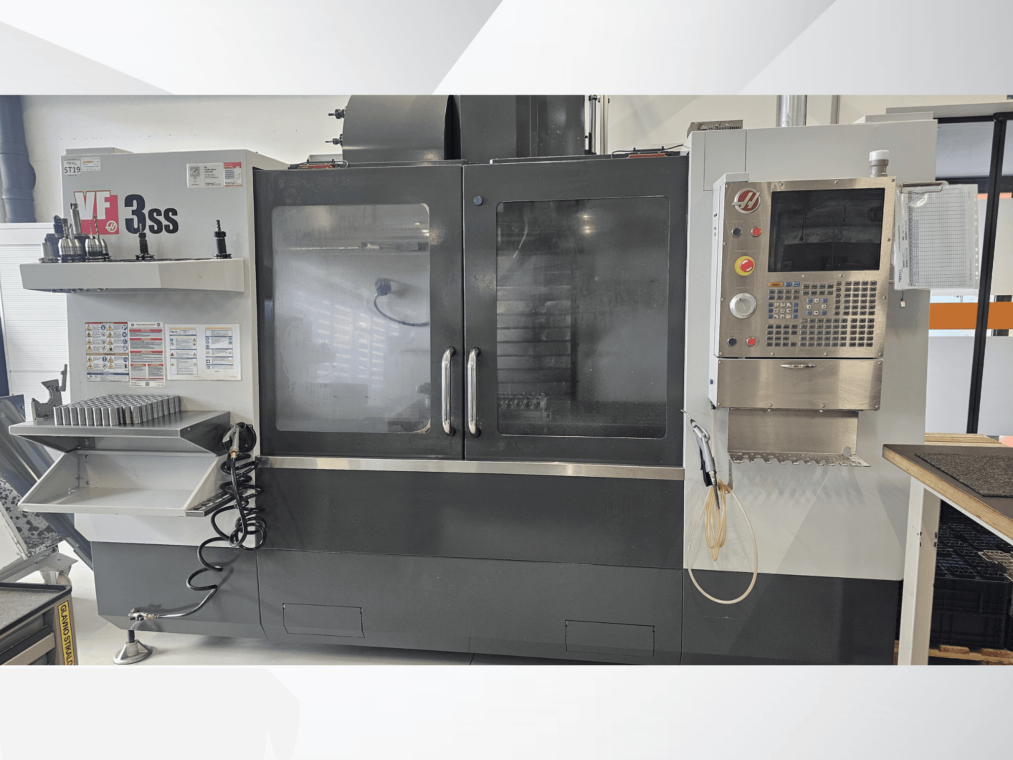 HAAS VF-3SS -pystytyöstökeskus, etukuva, jossa on ohjauspaneeli, työkaluhylly ja suuri lasiovi.