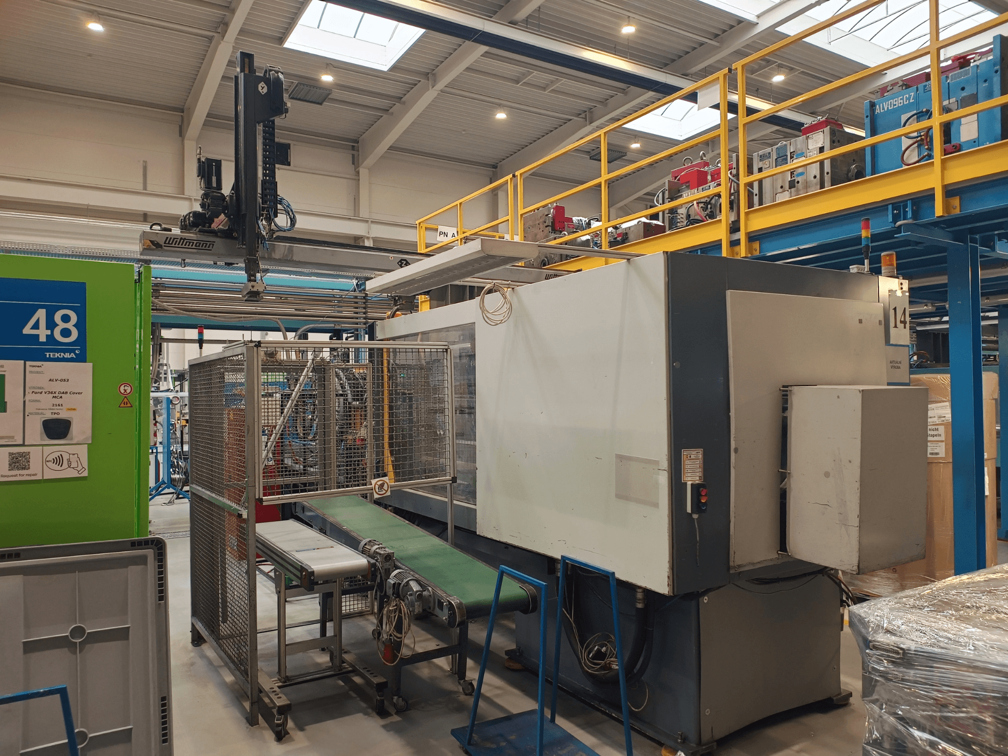 Winmonin teollisuusautomaatiokone, sivukuva, jossa näkyy kuljetinhihna, ohjauspaneeli ja turvahäkki tehdasympäristössä.