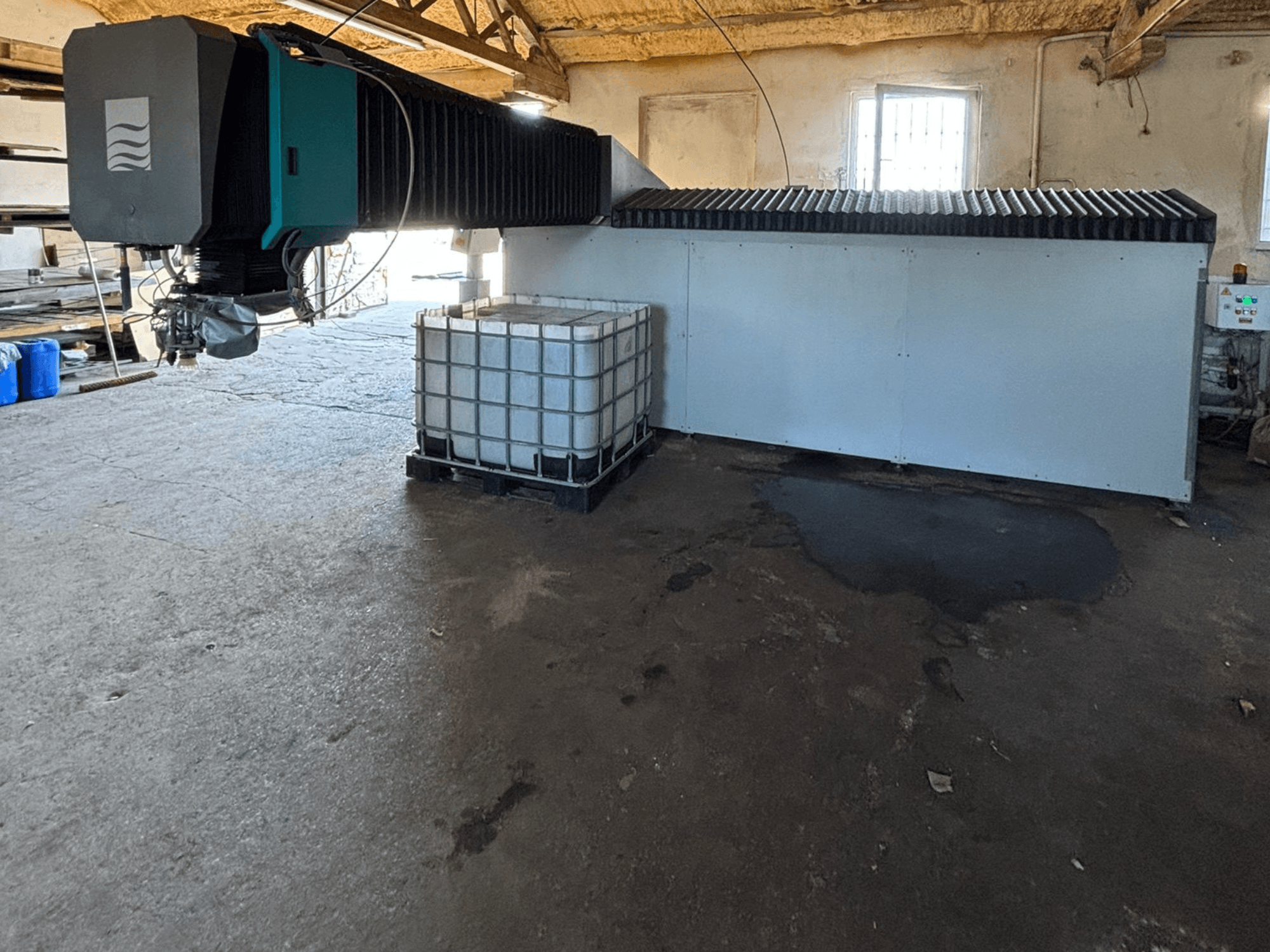 Teollisuuden vesisuihkukone korjaamolla, sivukuva, suuri vesisäiliö ja ohjauspaneeli näkyvissä sen vieressä.