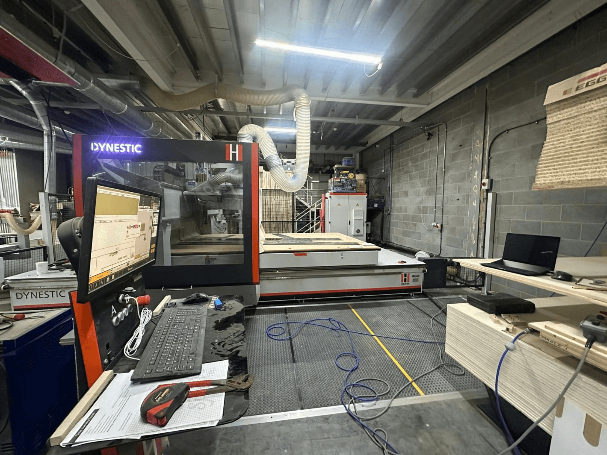 HOLZHER Dynestic 7535 -puuhiomokone työpajassa, ohjauspaneeli, näyttö ja materiaalit työpöydällä, etukuva.