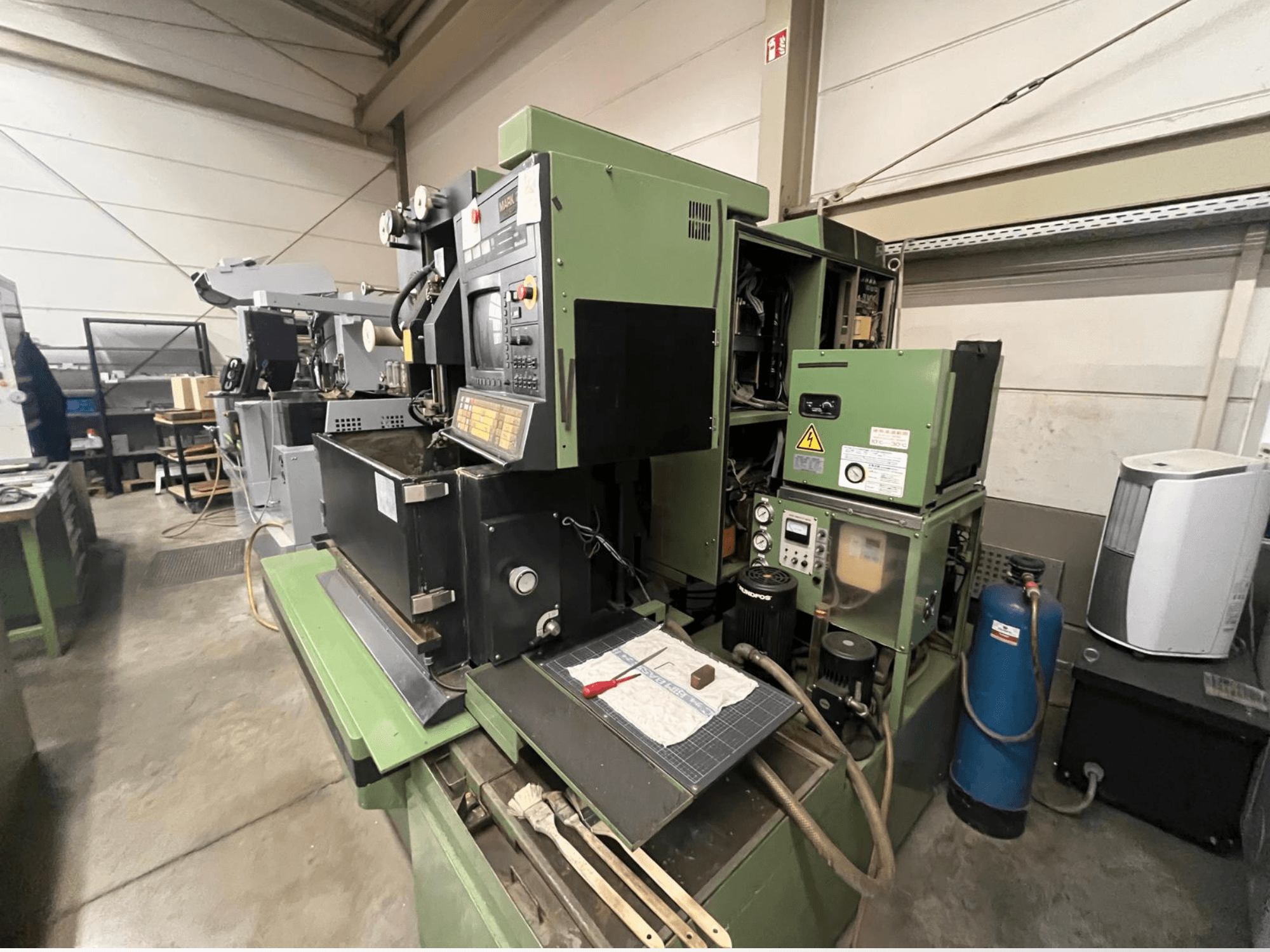 Vihreä teollisuuskone, jossa on ohjauspaneeli, sivukuva; sisältää hydrauliset komponentit ja työtilan pinnan työkaluineen.