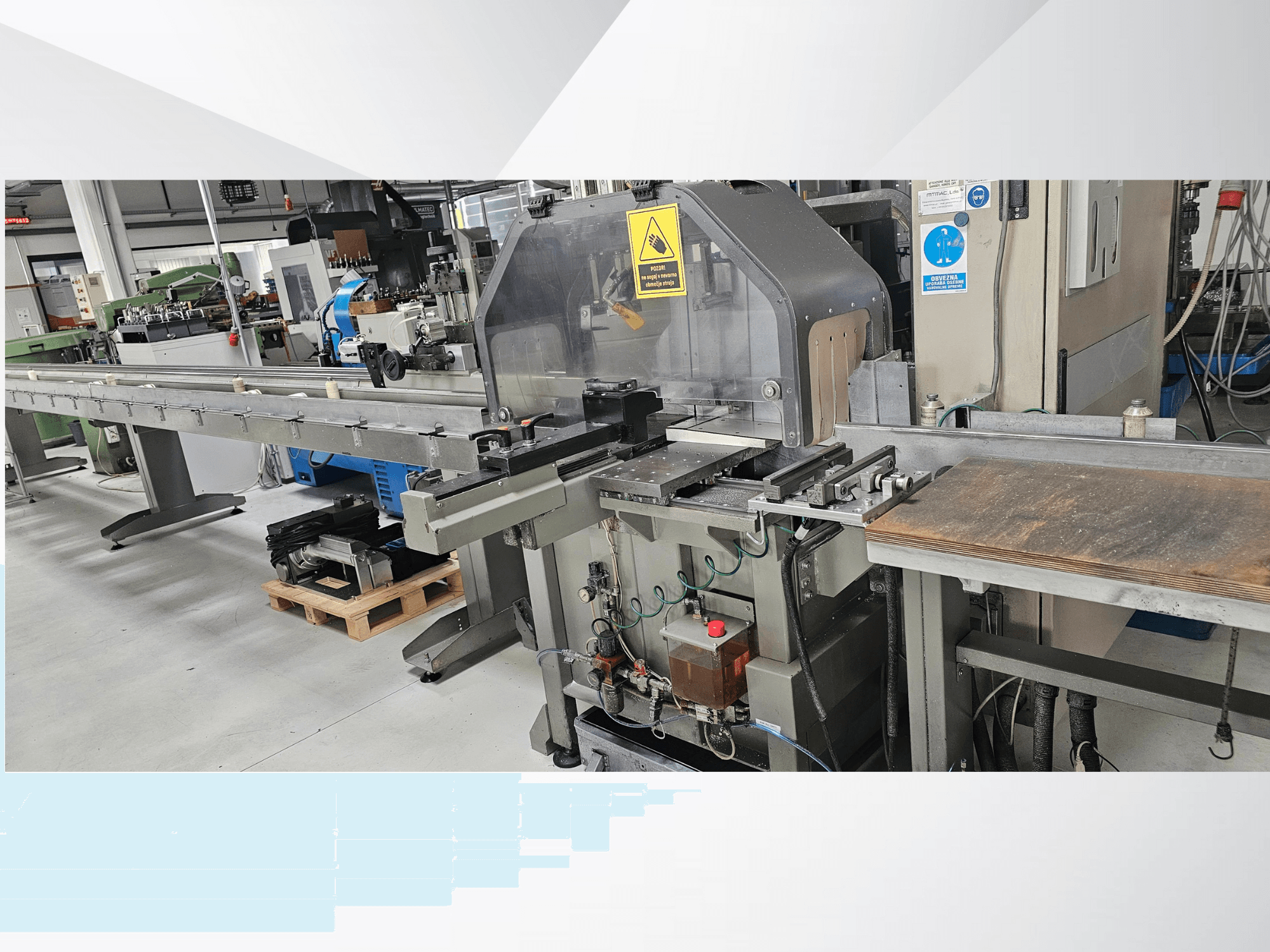 Teollisuusleikkauskone sivukuvasta, jossa on pitkä kuljetin, ohjauspaneeli ja turvavaroituksia.