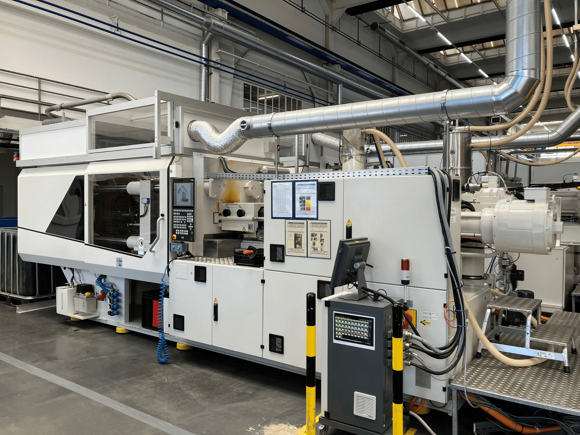 Etunäkymä teollisuuskoneesta, jossa on ohjauspaneeli, putket ja näyttöruudut, tyylikäs valkoinen muotoilu ja tekniset yksityiskohdat.