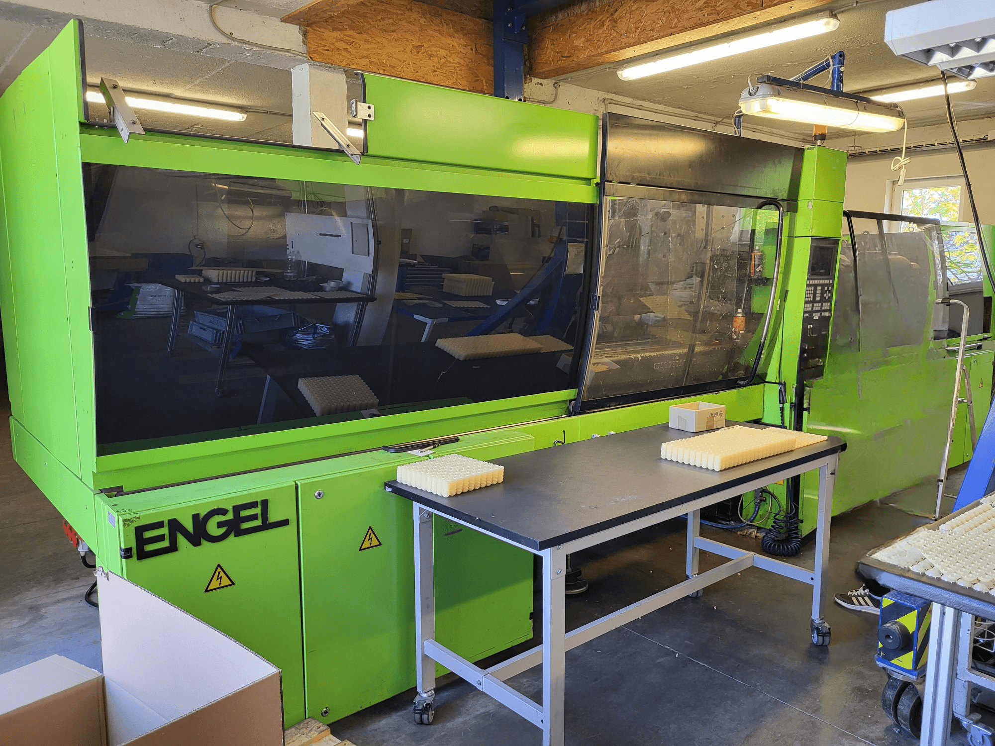 Green Engel ES1800/300HL -hydraulinen ruiskuvalukone edestä katsottuna, työpöydällä on pinottuja materiaaleja.