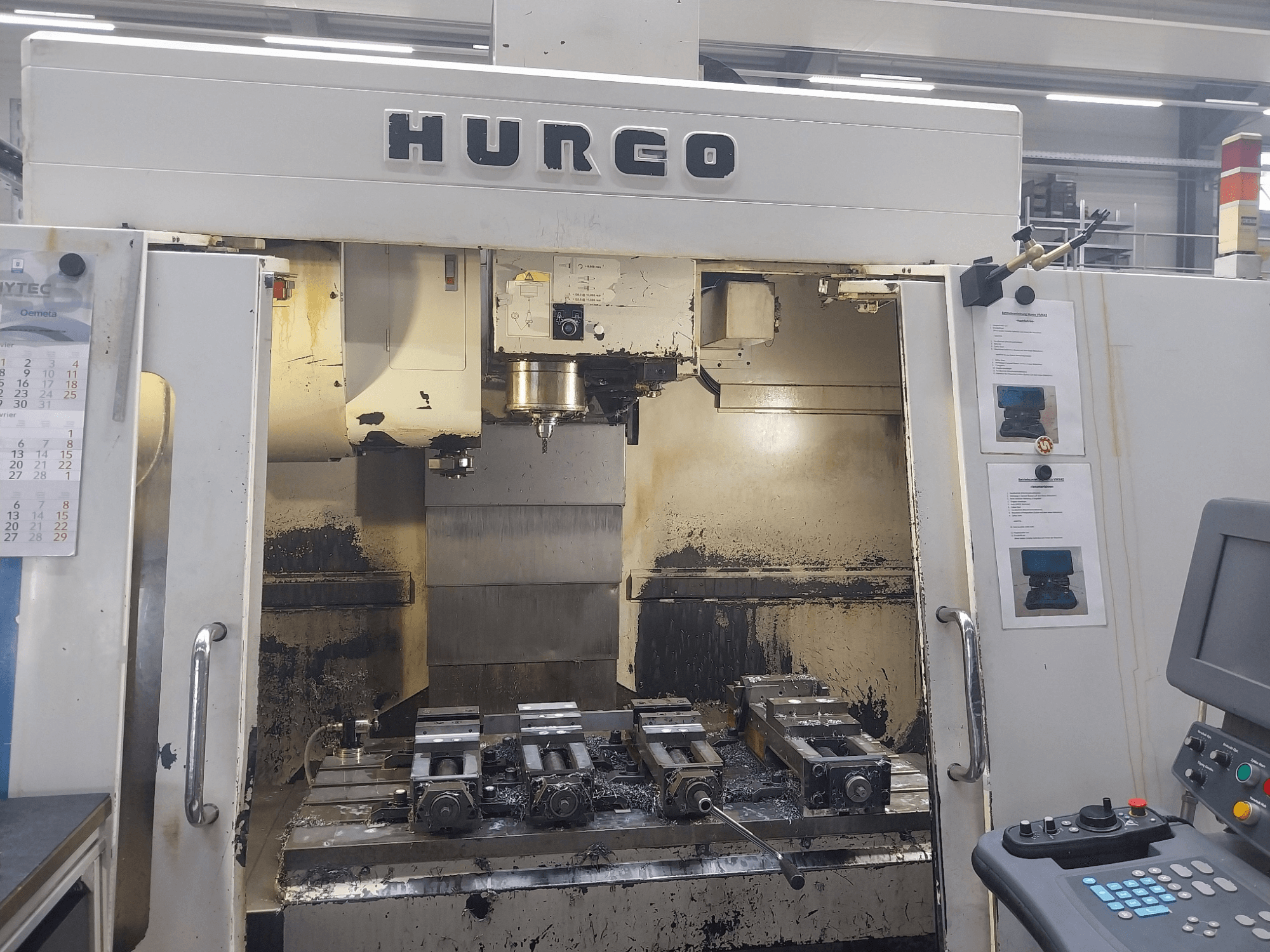 Hurco VMX 42 vertikaalinen työstökeskus, etukuva, jossa näkyy työpöytä kiinnikkeineen ja ohjauspaneeli, hieman kulunut kunto.