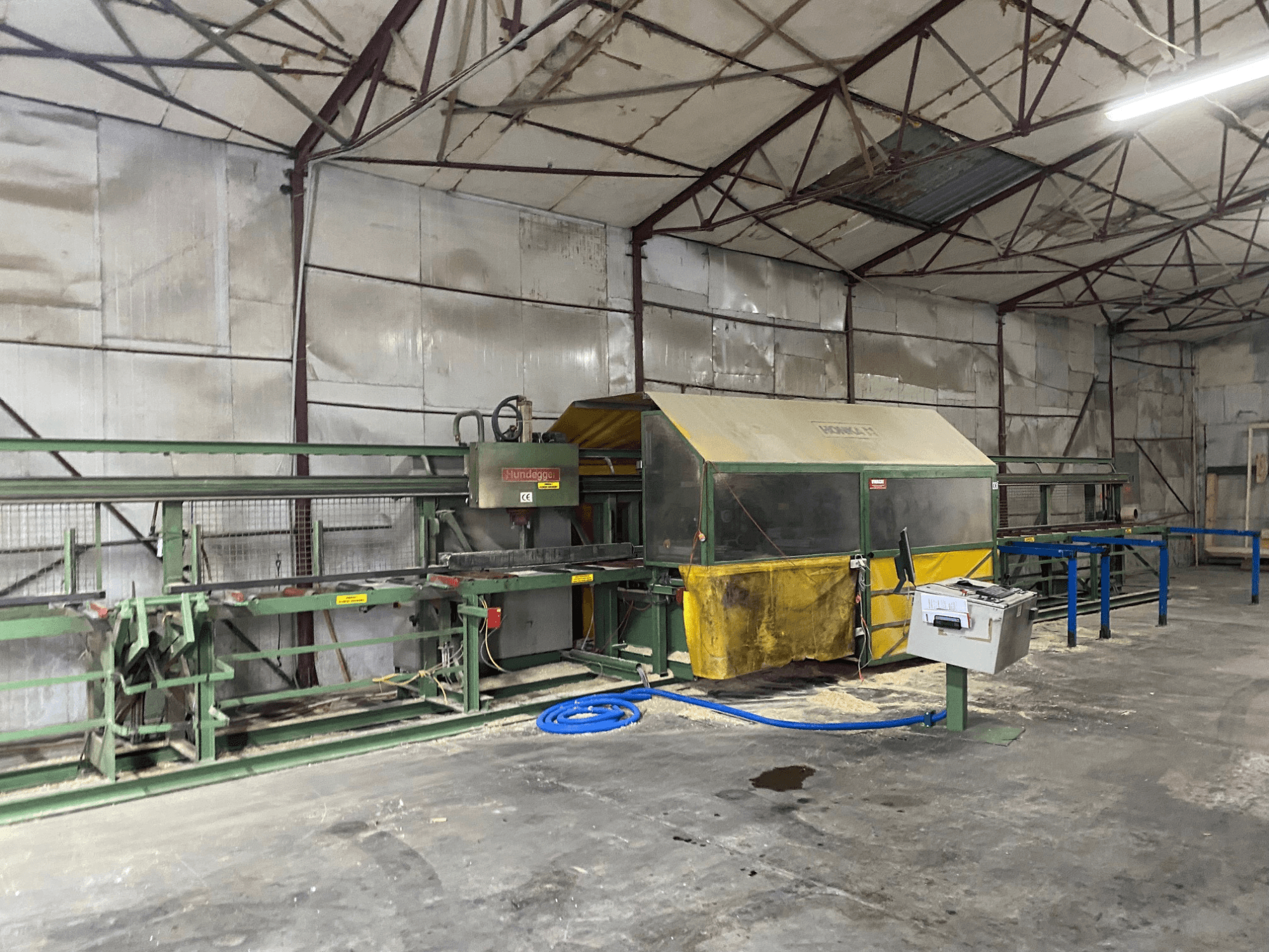 CNC-puuntyöstökeskus HUNDEGGER K1 työpajassa, sivukuva, jossa koneet, hallintalaitteet ja sahanpuru lattialla.