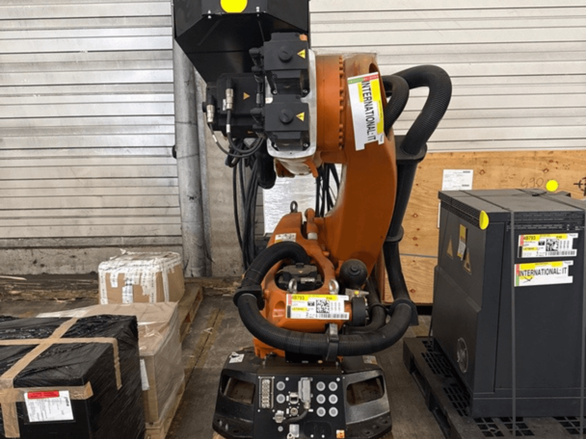 KUKA KR 210 R2700 -robottivarsi edestä katsottuna, esillä kuormalavalla pakkausten ja laitteiden vieressä.