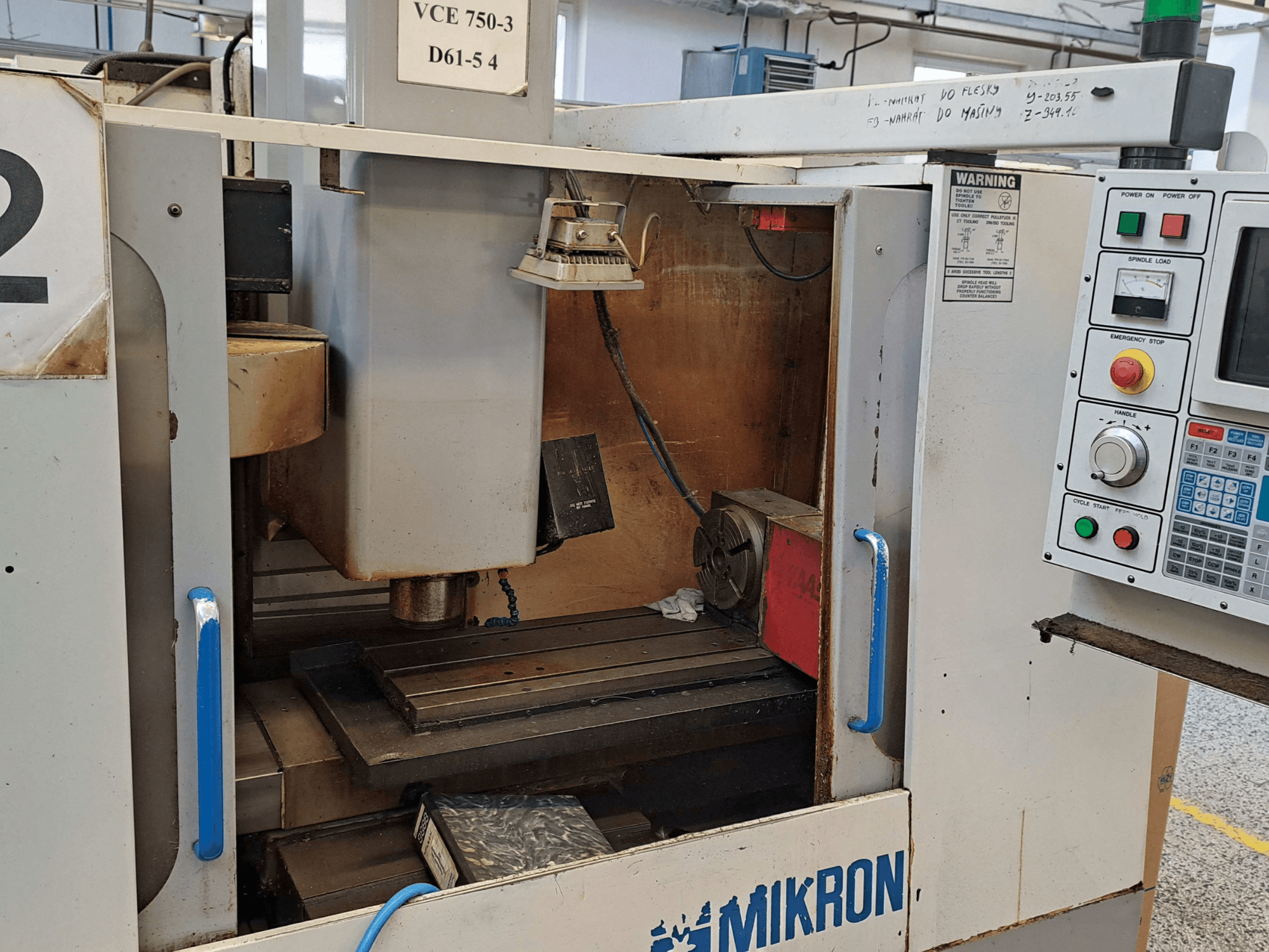 Mikron VCE 750-3 -jyrsinkoneen etukuva, jossa näkyy kara, ohjauspaneeli ja työpöytä teknisine yksityiskohtineen.