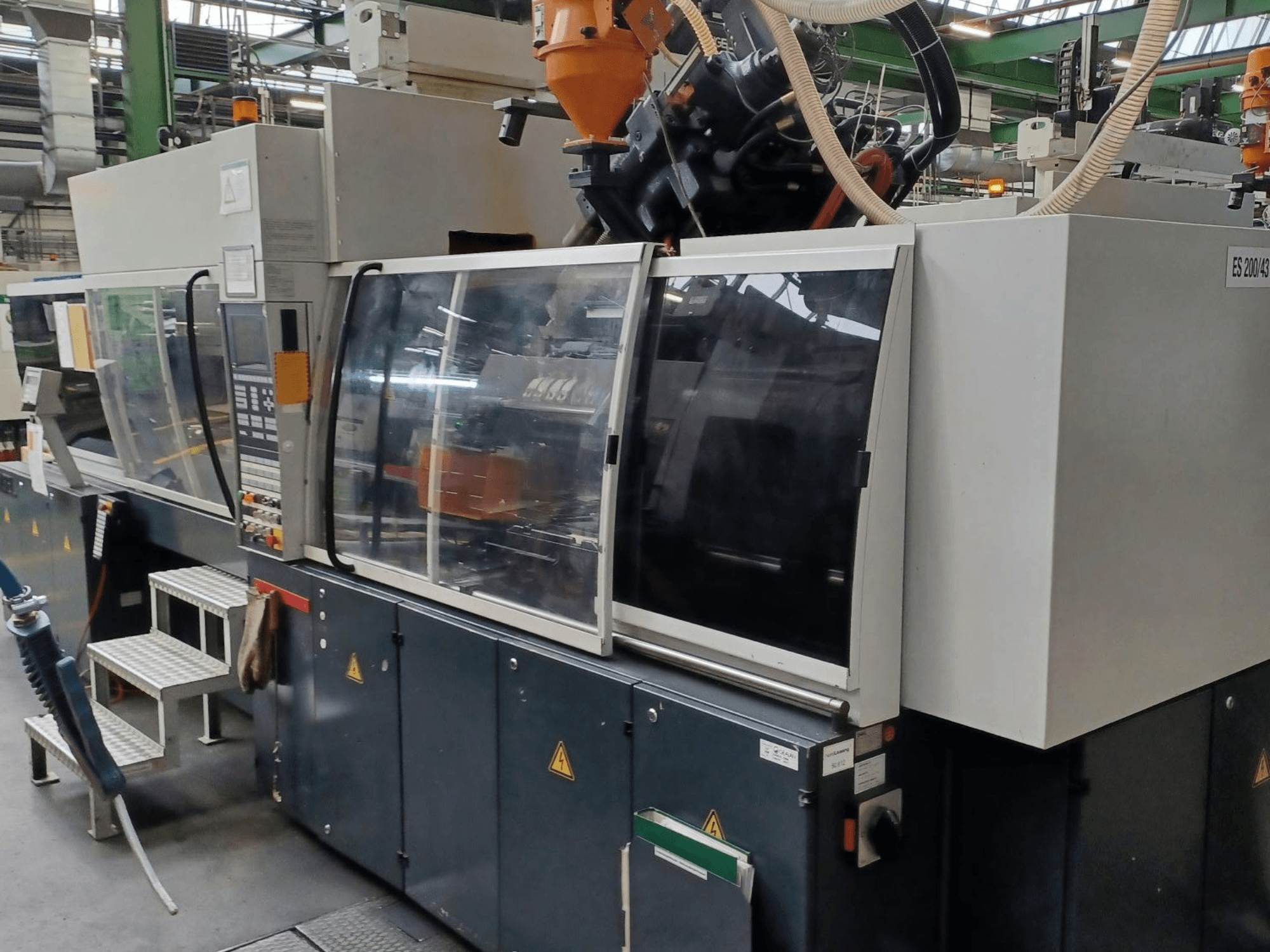 Etukuva muovin ruiskuvalukoneesta, merkki ja malli tuntematon, jossa on läpinäkyvät turvaovet ja ohjauspaneeli.