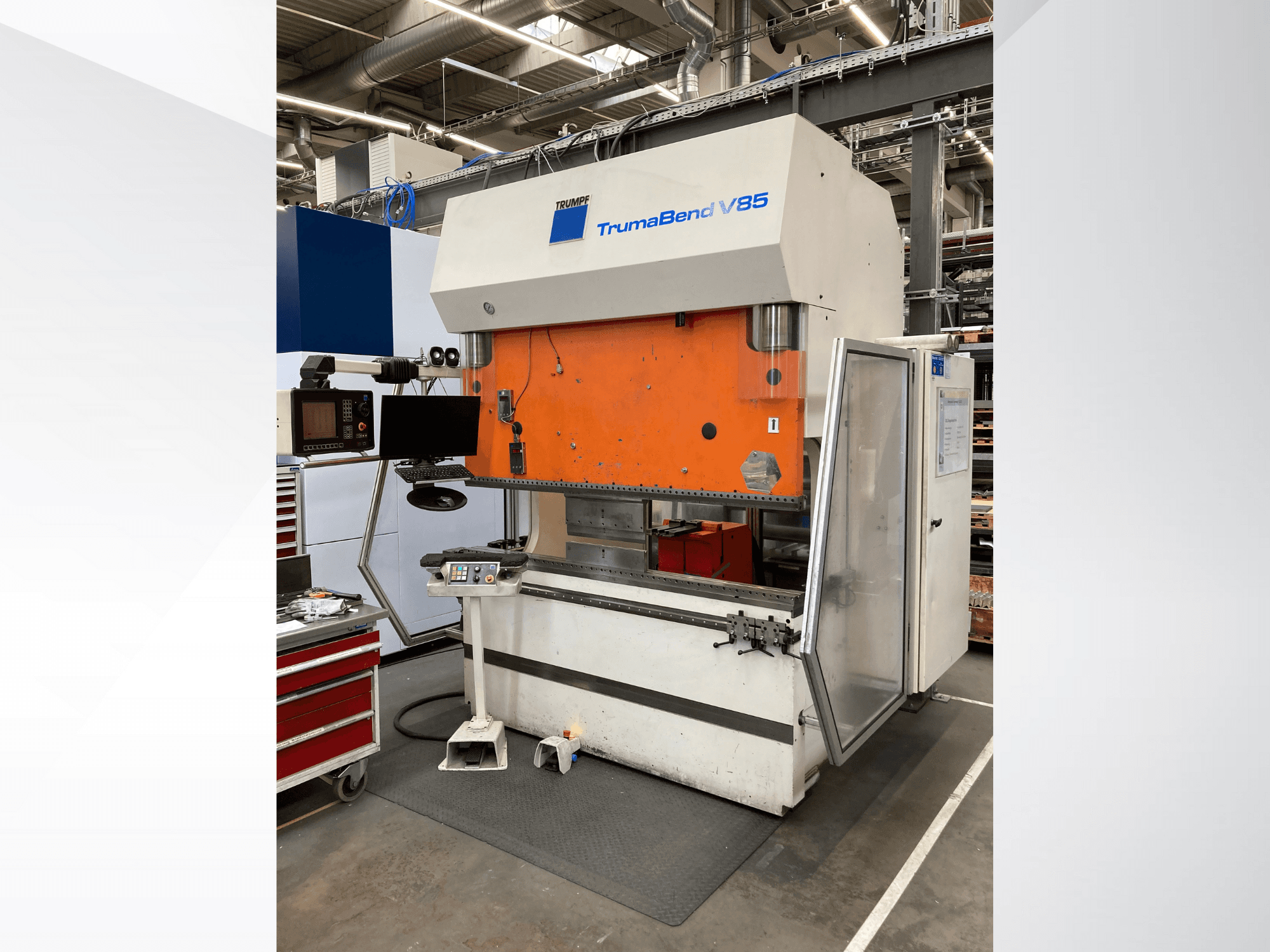 TruMatic V85 -taivutuskone tehtaalla, jossa on oranssi etupaneeli, ohjausnäyttö ja avoin sivuovi, sivukuva.